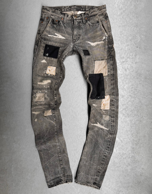 The Mihara Yasuhiro AW10 Double-pockets Repair Patchwork Selvedge Denim features a distressed gray wash, black, beige, and striped fabric patches, visible wear, frayed edges, and worn spots—showcasing bold Japanese streetwear style.