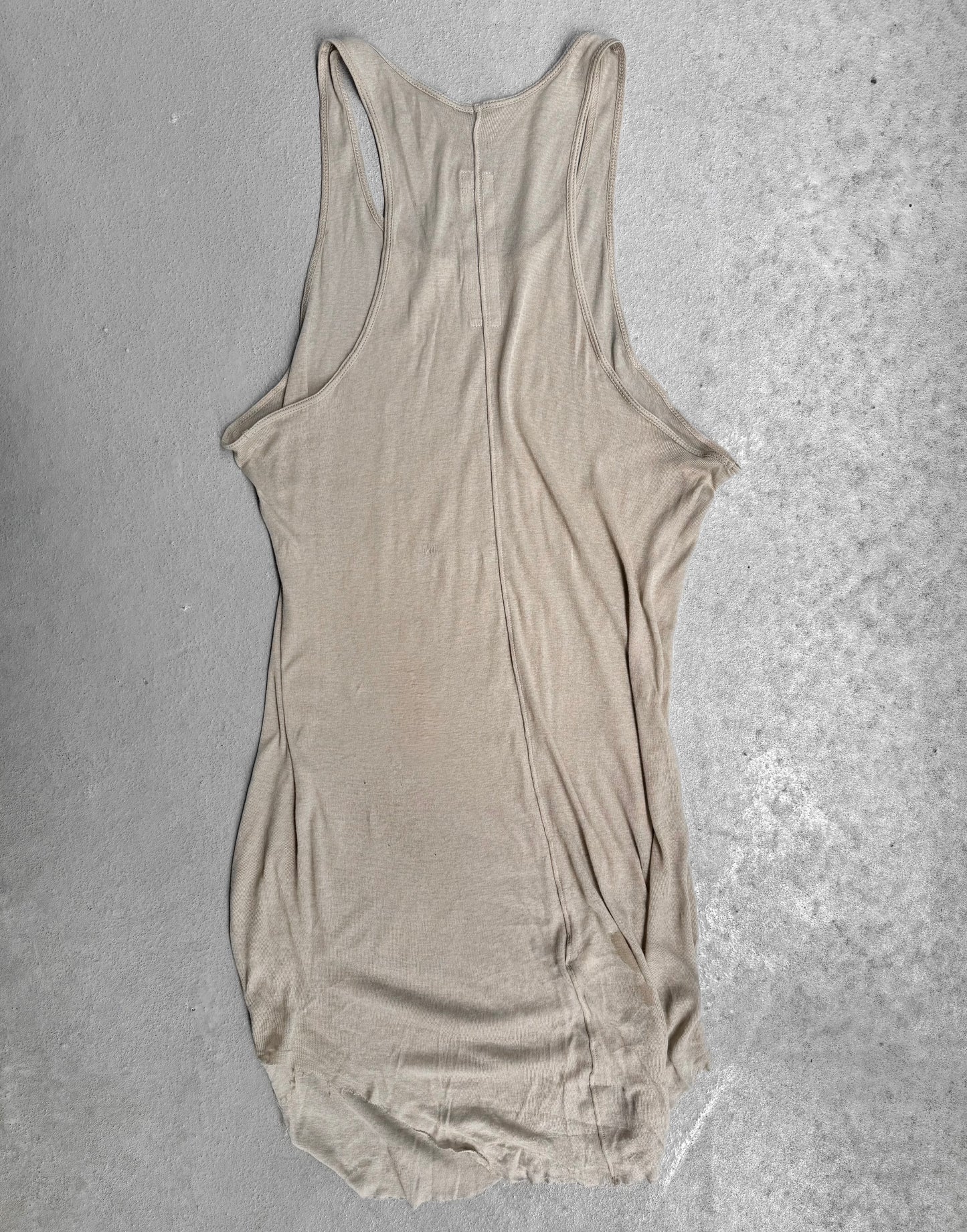 The Rick Owens SS24 “LIDO” Pearl Sheer D-Flap Tank Top, featuring a racerback and sculptural silhouette, is displayed flat on a light gray concrete surface. The fabric is slightly wrinkled with uneven edges.