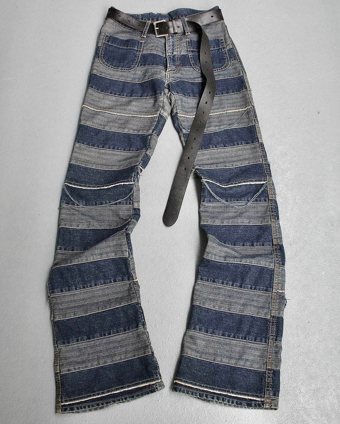 The Hysteric Glamour Early 00s ‘Kinky’ Blue Hagi Flare Denim features alternating light and dark denim stripes, a punk rock style, multiple pockets, and includes a black belt. The jeans are styled like those from Hysteric Glamour and laid out on a light surface.