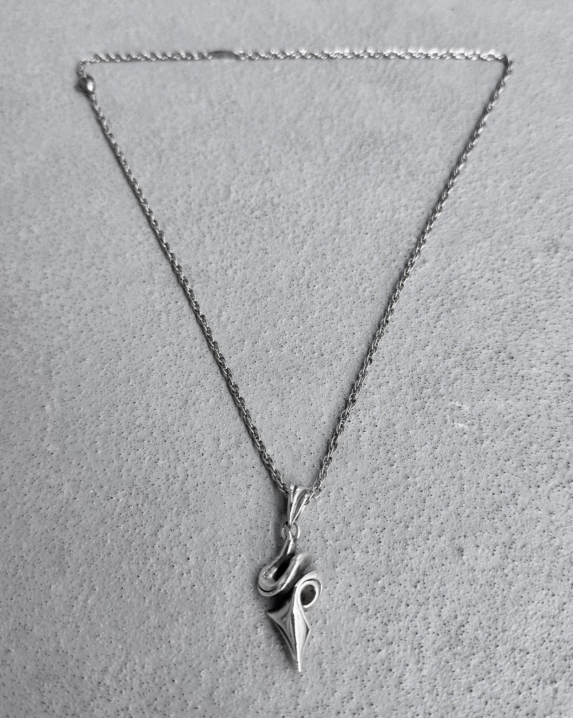 The M’s Collection (BLESS) Early 00s Silver Tribal Twist Pendant Chain by BLESS, featuring a snake-shaped design with a pointed tail, is elegantly displayed on a textured gray surface. This piece exemplifies cable jewellerys commitment to sustainability in conceptual fashion.