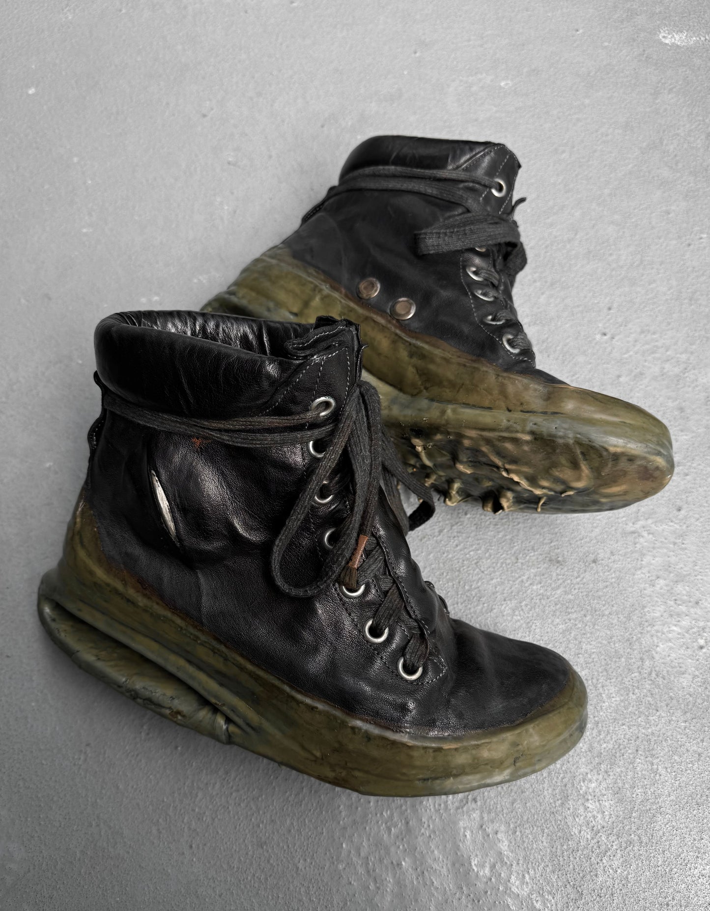 A pair of DRIEW Carol Christian Poell ‘AM/2685P ROOMS-PTC/12’ black high-top kangaroo leather sneakers (Size 6, EU 41.5-42) with thick translucent green soles, light wear, scuffs, creases, and loosely tied black laces rest on a gray surface.