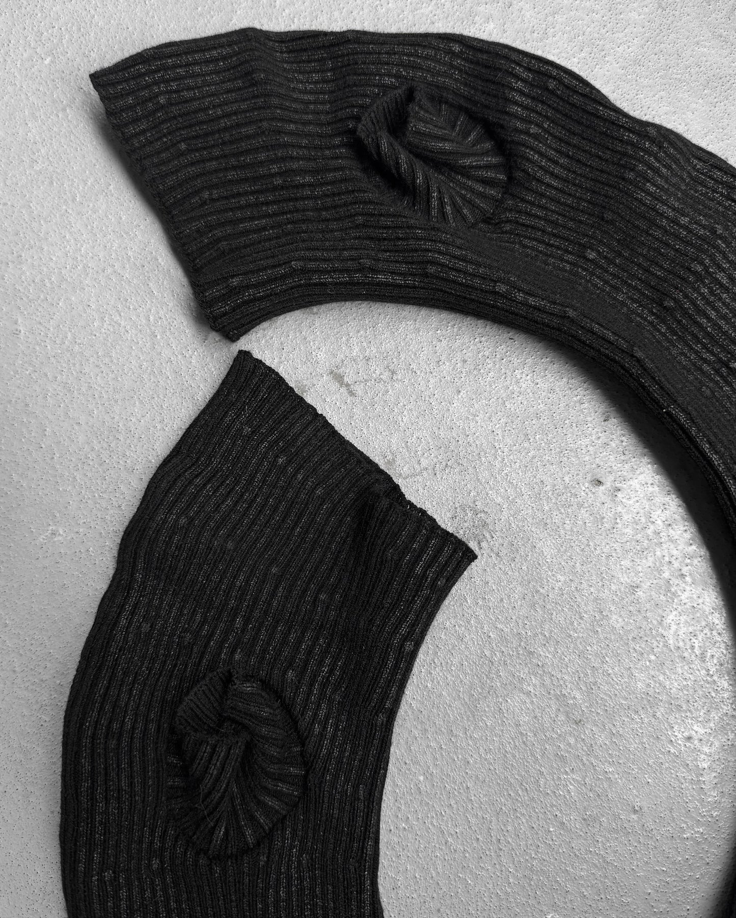 Two black, curved wax coated gloves from DRIEW’s Julius_7 AW24-25 “rift;” line are displayed on a light surface. Their flawless one-size design and textured finish stand out in this black-and-white shot.