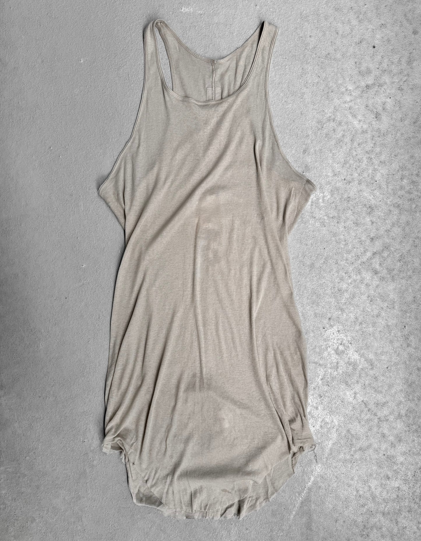 The Rick Owens SS24 “LIDO” Pearl Sheer D-Flap Tank Top is laid flat on a light gray textured surface, showing its soft, slightly wrinkled fabric, loose fit, and curved hem inspired by Rick Owens signature sculptural style.