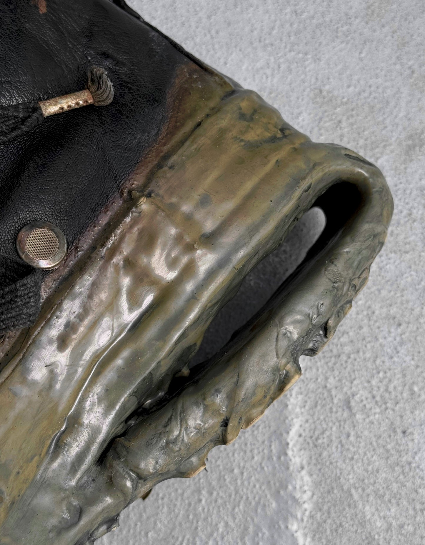 Close-up of DRIEW Carol Christian Poell ‘AM/2685P ROOMS-PTC/12’ object-dyed kangaroo leather sneakers, showing a weathered titanium handle and button detail against a textured gray surface.