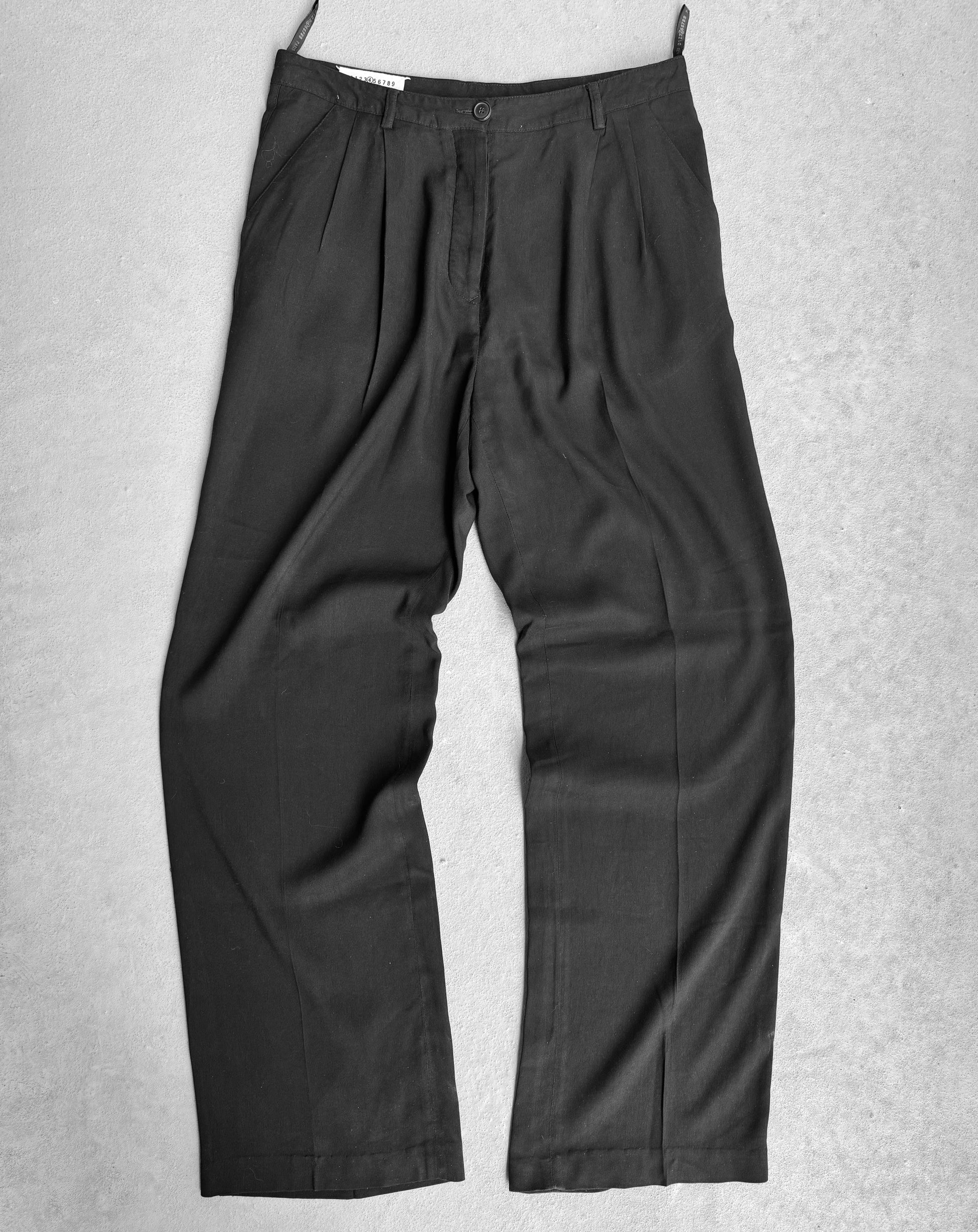 A pair of Maison Martin Margiela Early 00s Double Pleated Dress Pants in black features deconstructionist techniques against a light gray background, with pleats at the waist and straight legs, made from a lightweight fabric, merging avant-garde style with formal or office wear suitability.