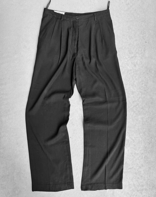A pair of Maison Martin Margiela Early 00s Double Pleated Dress Pants in black features deconstructionist techniques against a light gray background, with pleats at the waist and straight legs, made from a lightweight fabric, merging avant-garde style with formal or office wear suitability.