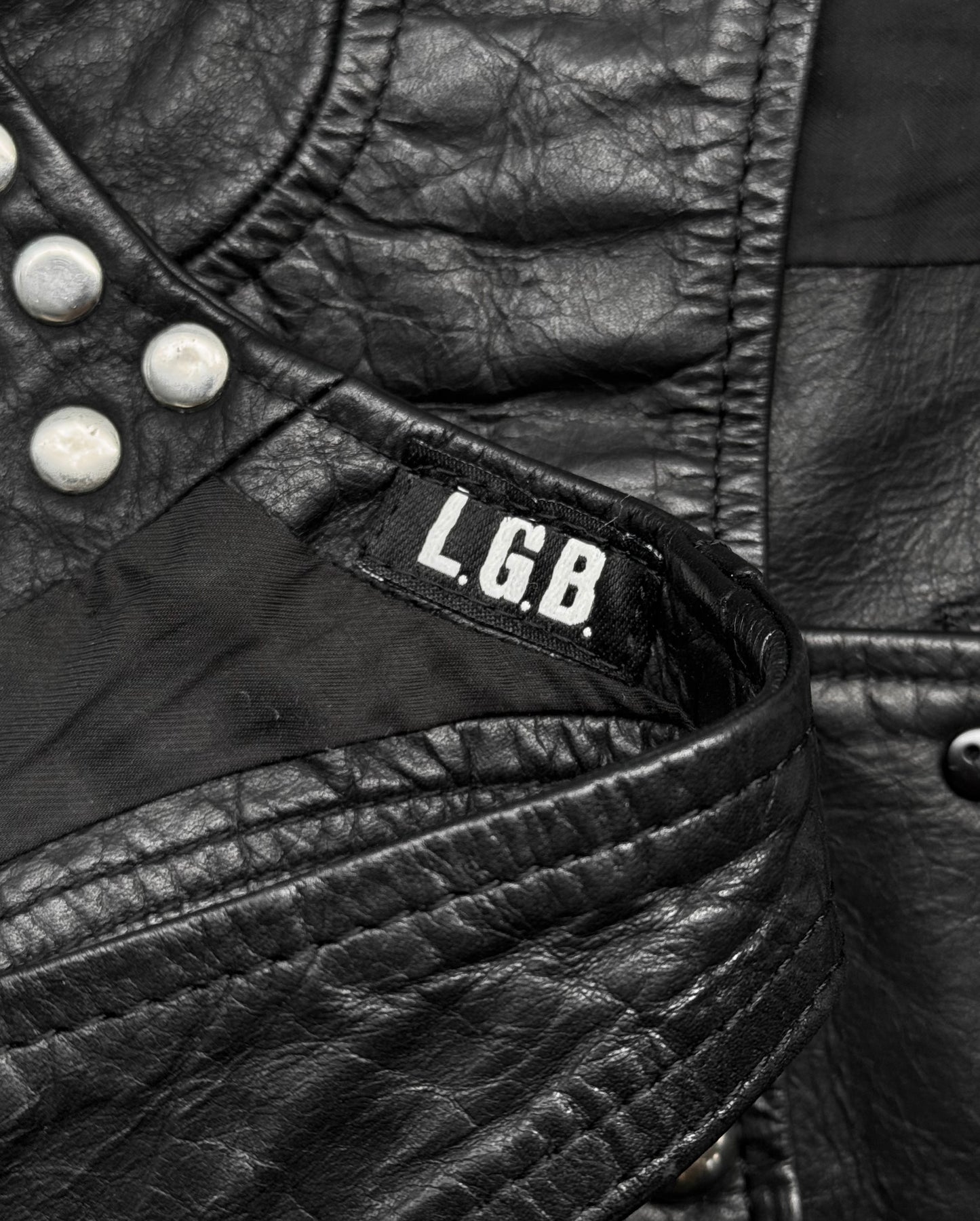 Close-up of a L.G.B Early 00s Calfskin Leather Studded Mini-vest in black, size medium, featuring silver studs, white L.G.B tag, textured detailing, visible stitching, light discolouration; condition rated 8/10.