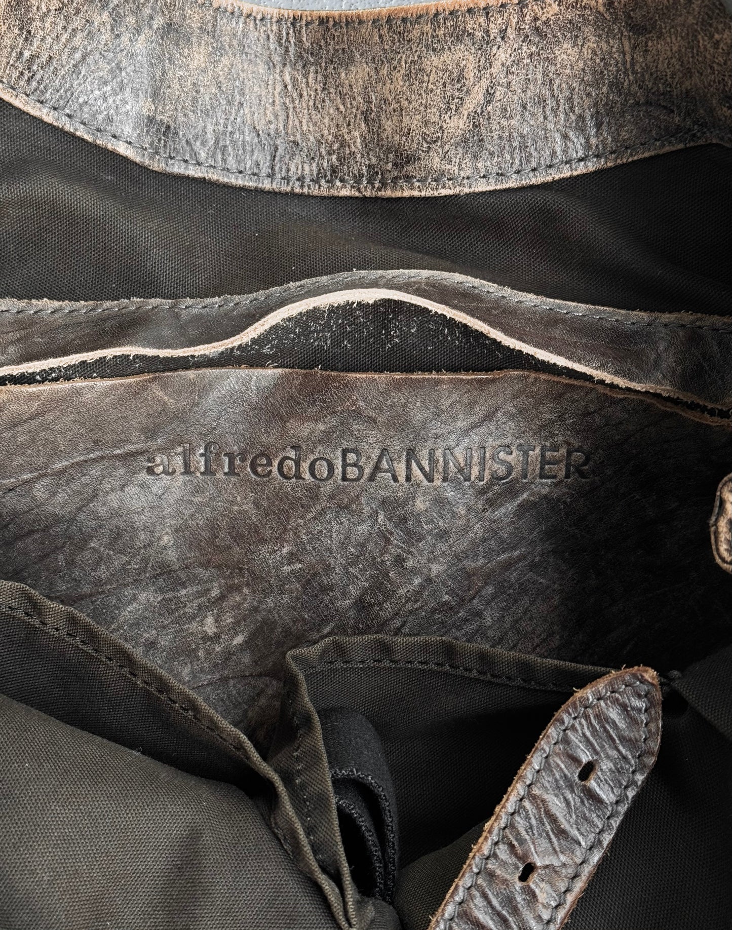 A close-up of a worn leather tote bag with embossed alfredoBANNISTER text. The Japanese cowhide from the early 00s exhibits aging, displaying a textured and distressed look that highlights its contemporary design influences.
