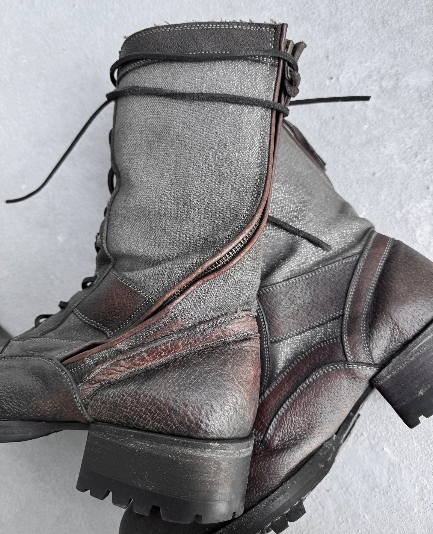 Close-up of Kyoji Maruyama Early 00s Brown Tornado Zip Combat Boots with rugged soles and textured surfaces, blending brown and gray tones with black laces and side zippers, reminiscent of Japanese fashion and evoking the vintage charm of a mouton jacket.