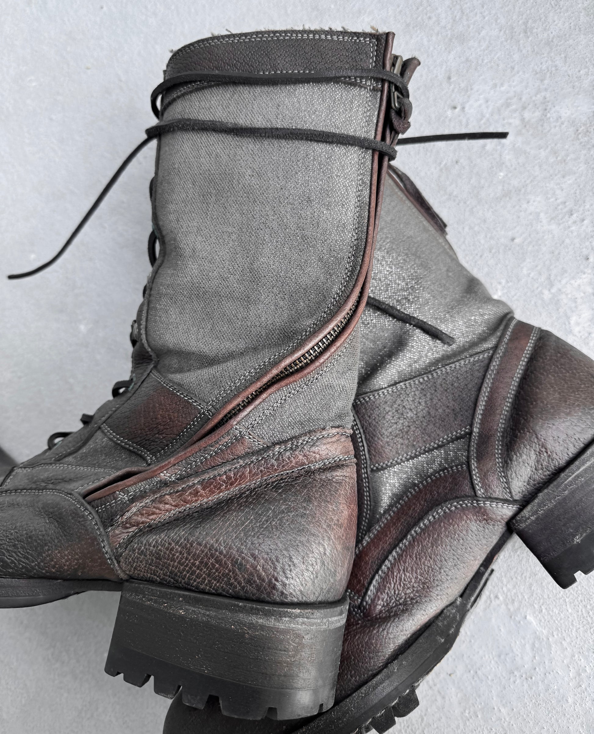 Close-up of Kyoji Maruyama Early 00s Brown Tornado Zip Combat Boots with rugged soles and textured surfaces, blending brown and gray tones with black laces and side zippers, reminiscent of Japanese fashion and evoking the vintage charm of a mouton jacket.