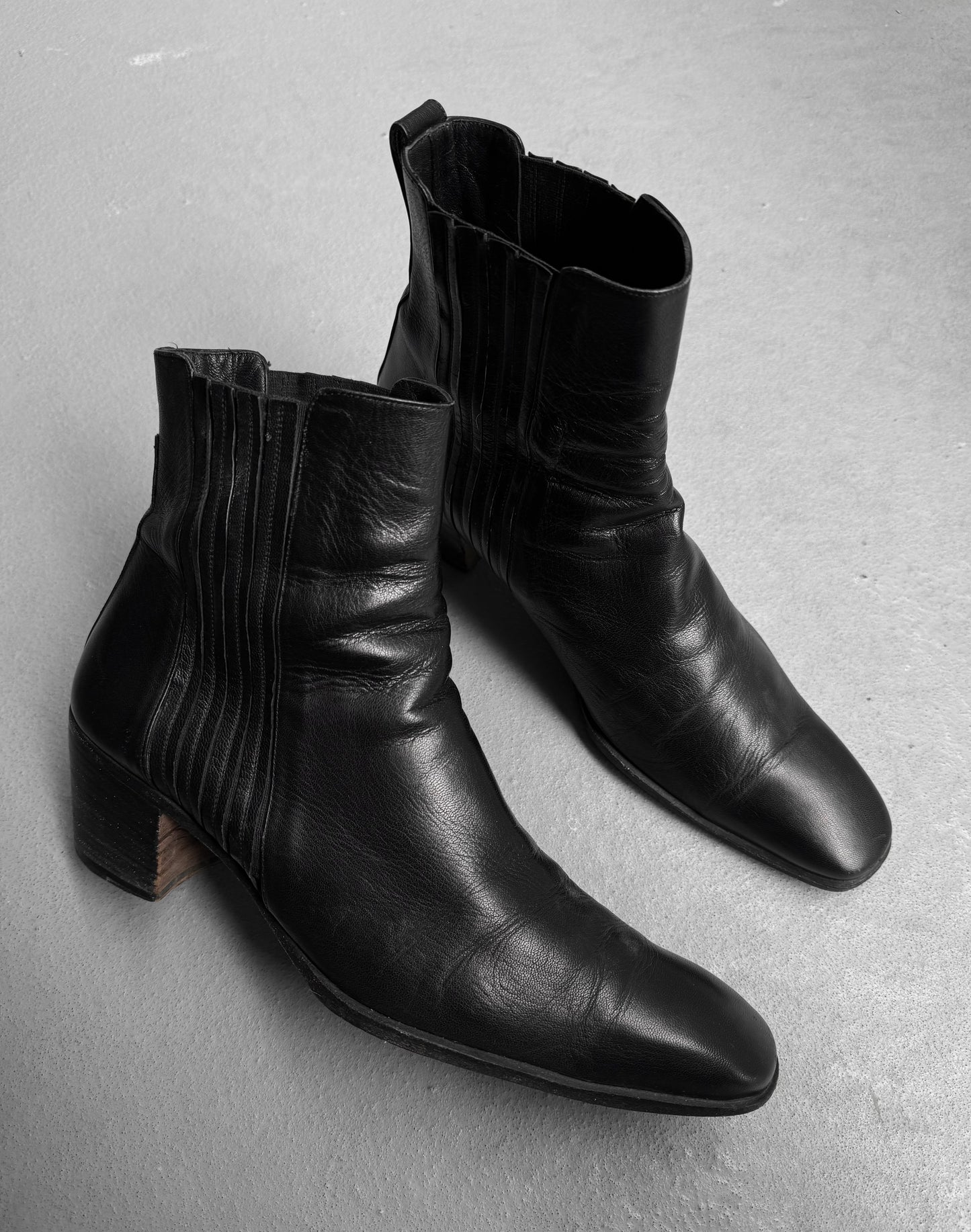 A pair of Saint Laurent Paris YSL Rive Gauche SS04 by Tom Ford ‘Johnny’ leather boots with 40mm stacked heels and side stitching, in black, displayed on a light gray floor.