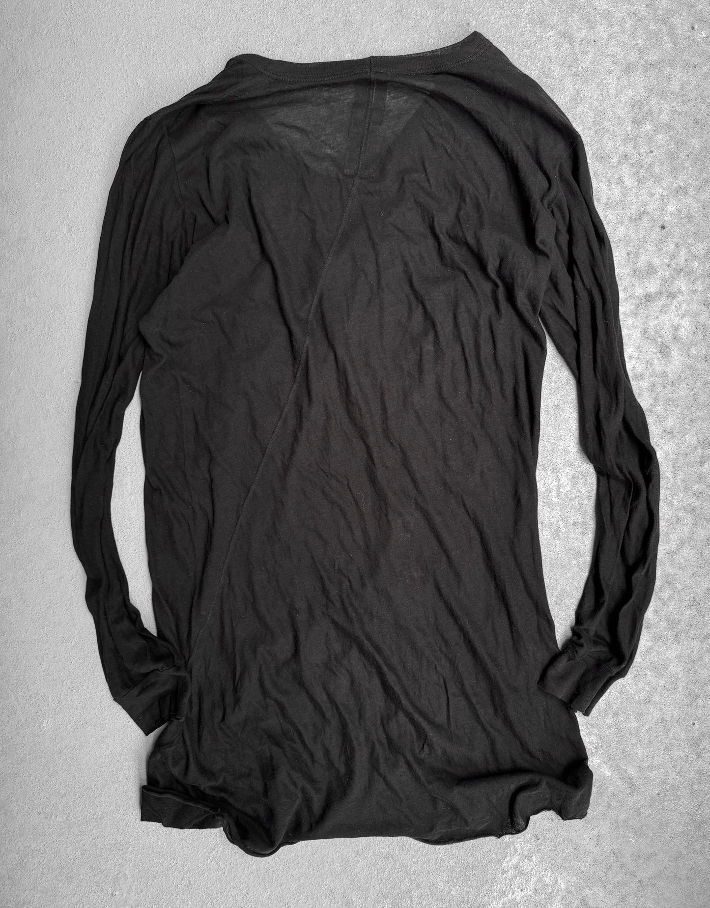 The Rick Owens SS10 “RELEASE” black sheer long-sleeve shirt lies flat and inside-out on a light gray textured surface, its wrinkled, semi-transparent fabric evoking the edgy, avant-garde style iconic to Rick Owens.