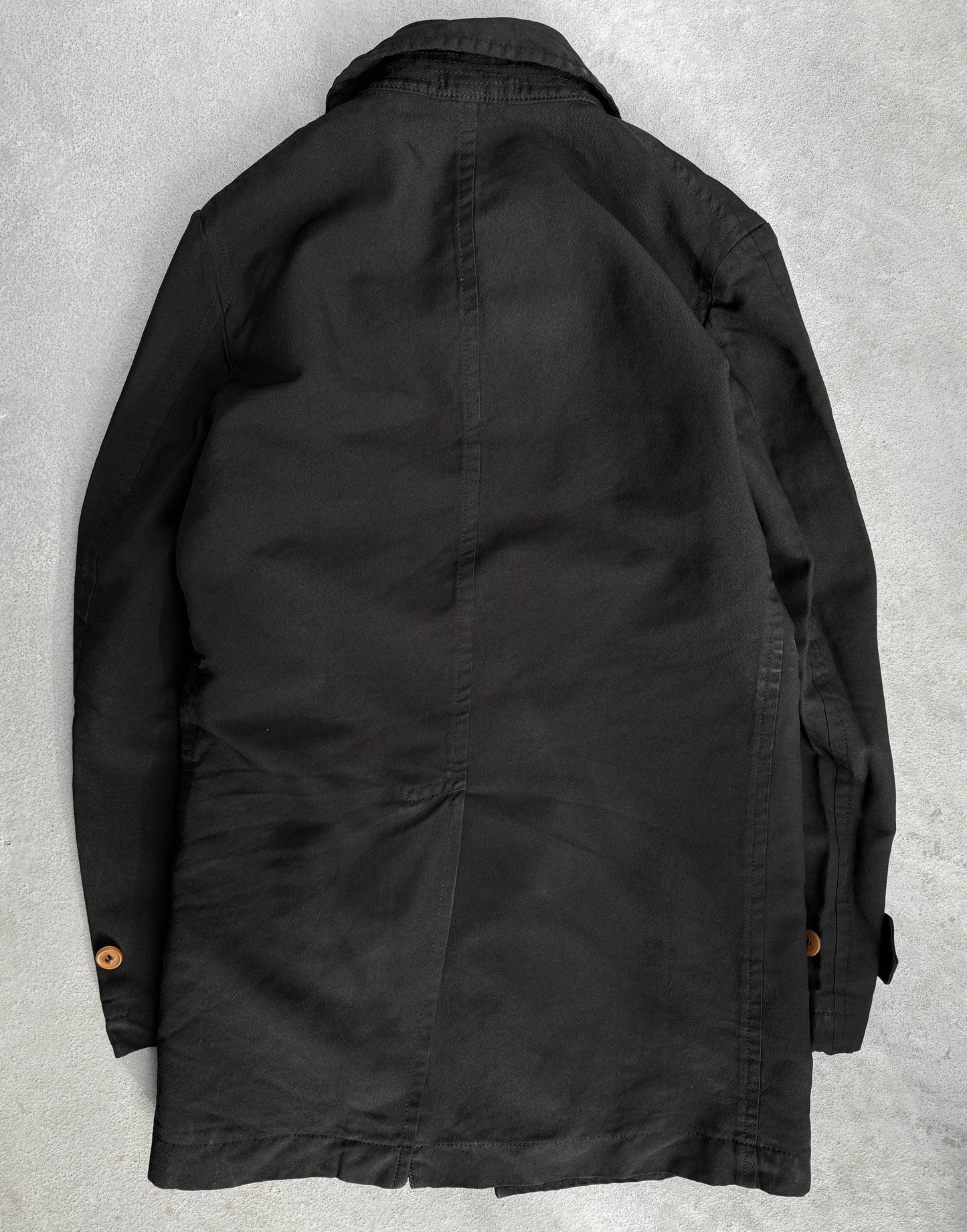 A COMME des GARÇONS HOMME DEUX Early 00s Reversible Button-up Coat is displayed on a gray surface. The coat, with its collar, long sleeves, buttoned cuffs, and menswear-inspired design, showcases smooth fabric and tailored seams reflecting COMME des GARÇONS avant-garde fashion style.