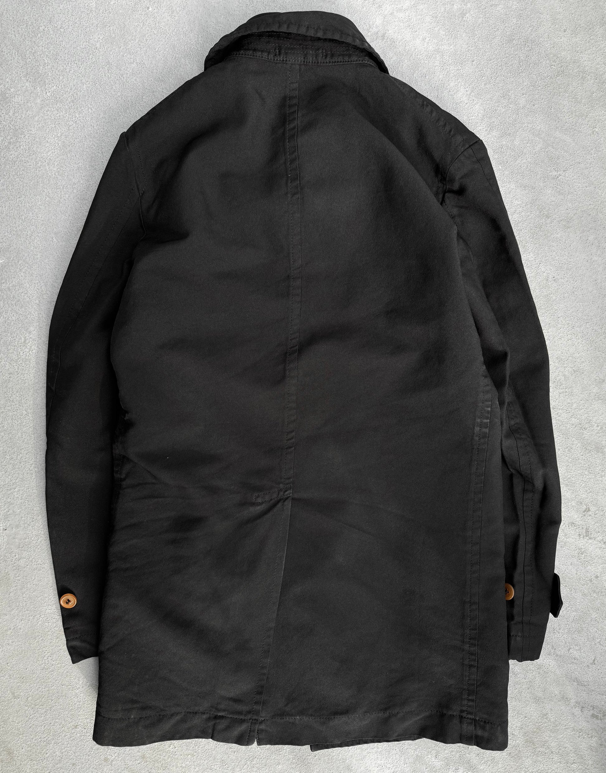 A COMME des GARÇONS HOMME DEUX Early 00s Reversible Button-up Coat is displayed on a gray surface. The coat, with its collar, long sleeves, buttoned cuffs, and menswear-inspired design, showcases smooth fabric and tailored seams reflecting COMME des GARÇONS avant-garde fashion style.