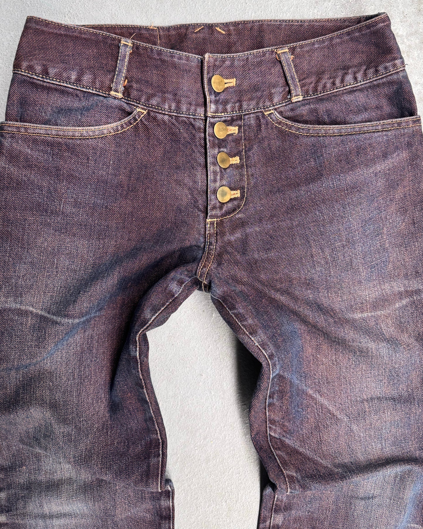 The Beauty:Beast Late 90s Over-dyed Articulate Bootcut Denim jeans lay flat, showcasing a Tokyo fashion vibe with a button fly, visible stitching, and slightly faded texture, merging classic style with avant-garde design on a light neutral background.