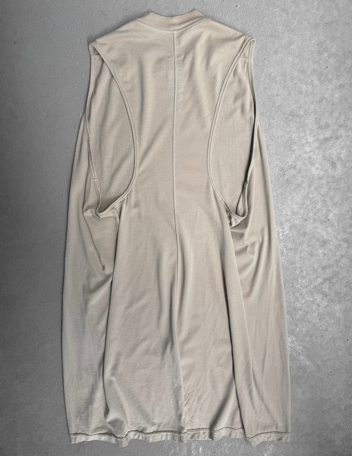 The Rick Owens DRKSHDW AW18 “SISYPHUS” Pearl Racer Tank Top is laid flat on a gray textured surface, showcasing its unique seam lines and draped fabric that reflect Rick Owens’ modern gothic grunge style.
