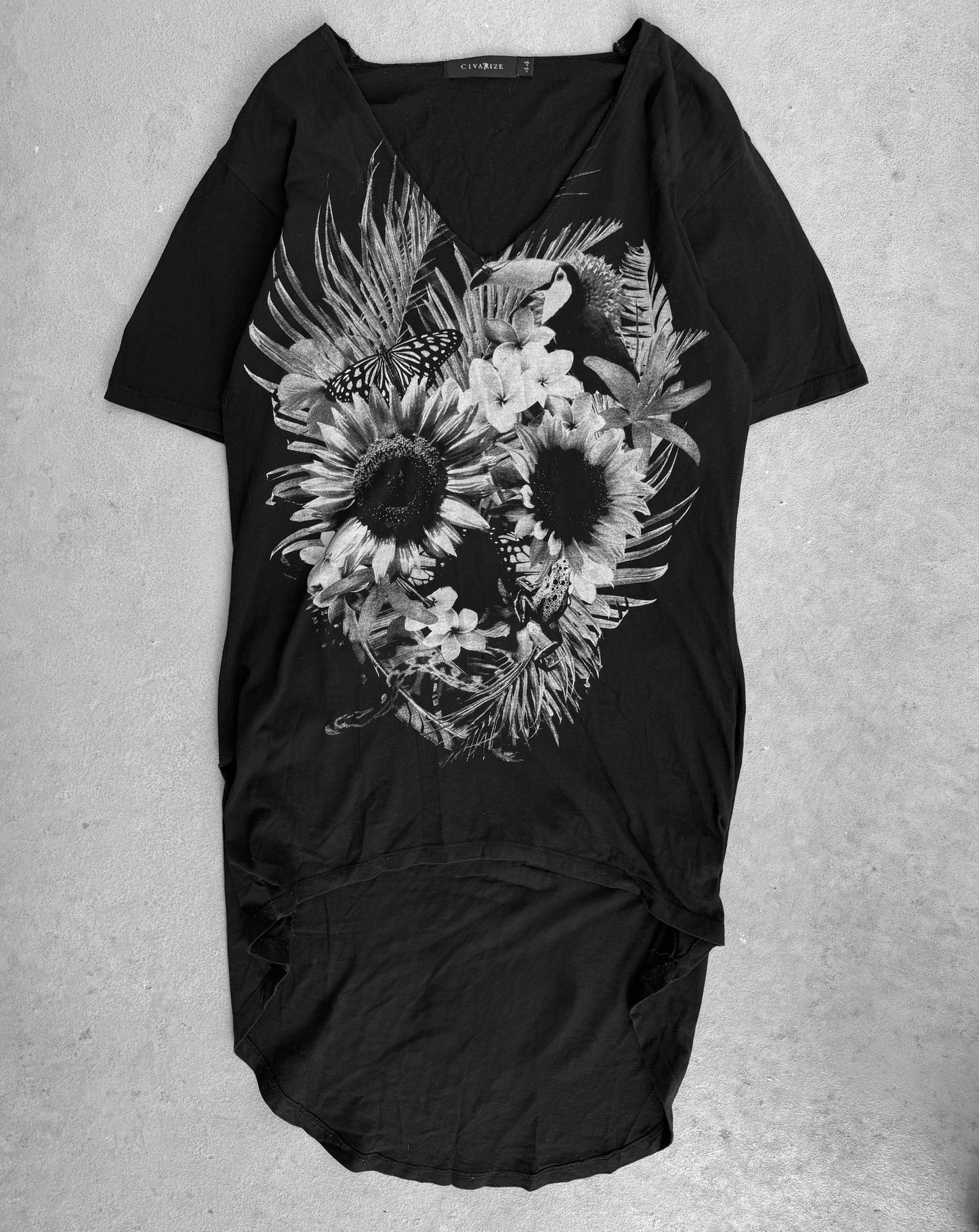 The CIVARIZE Early 00s ‘Floral Skull’ Graphic Long Curve T-shirt features a Visual Kei-inspired grayscale floral skull design with sunflowers, lilies, leaves, and a butterfly. Ideal for alternative fashion fans, the black shirt is shown on a neutral background.