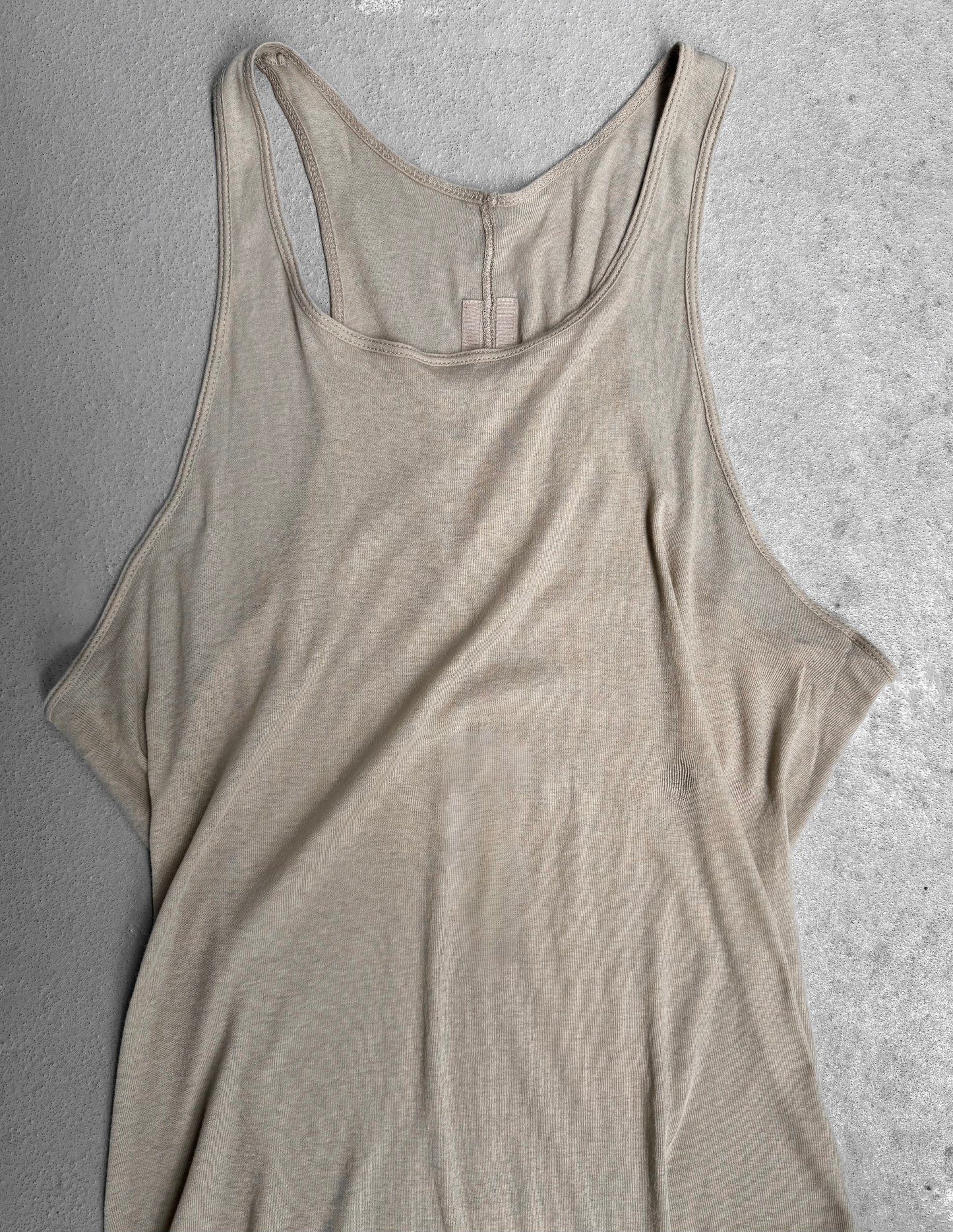 The Rick Owens SS24 “LIDO” Pearl Sheer D-Flap Tank Top, a beige sleeveless racerback style, is laid flat on a light gray textured surface.