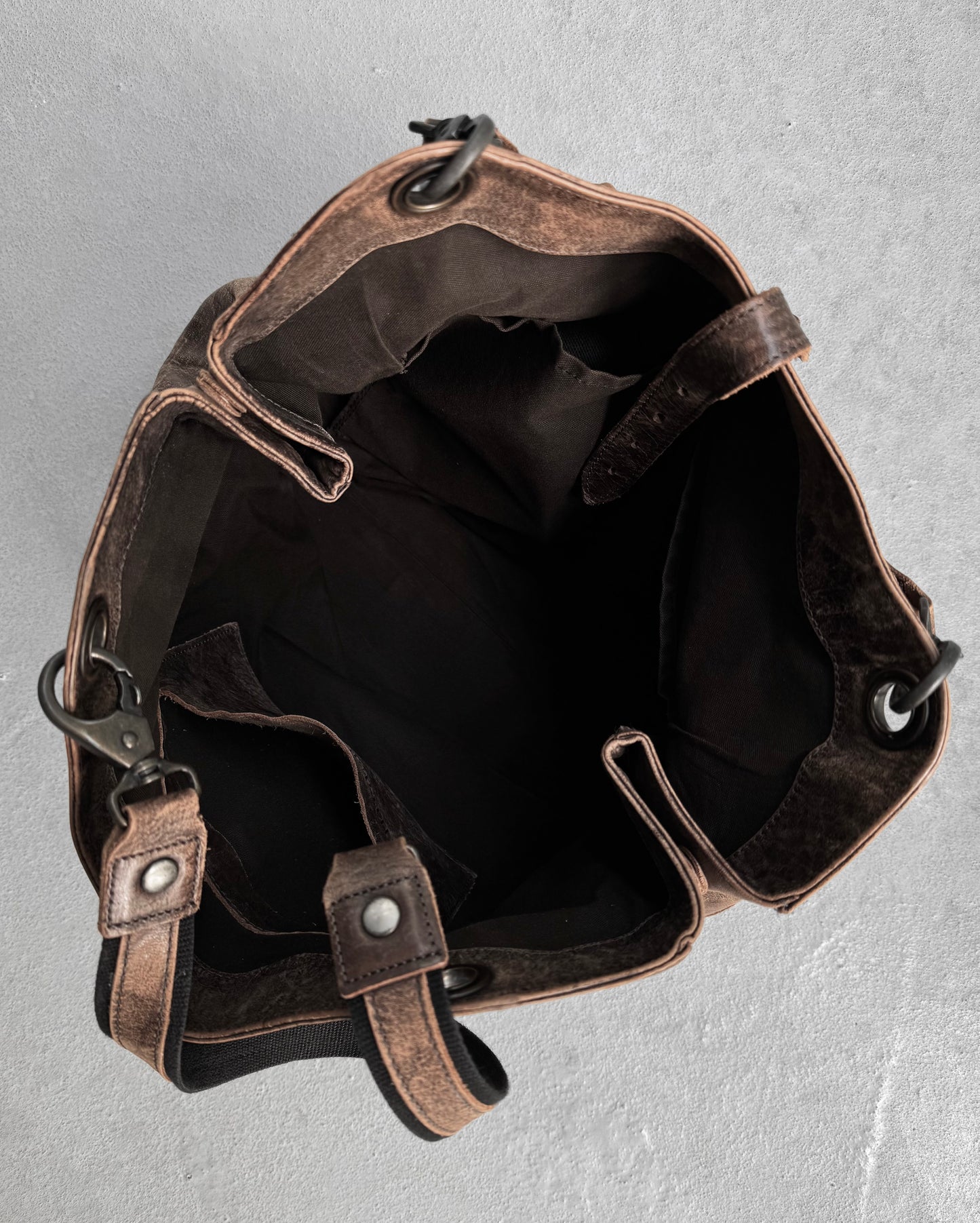 A top-view of the alfredoBANNISTER Early 00s Faded Brown Cowhide Tote Bag with metal grommets and leather straps. Its interior, featuring a dark fabric lining, highlights contemporary design elements.