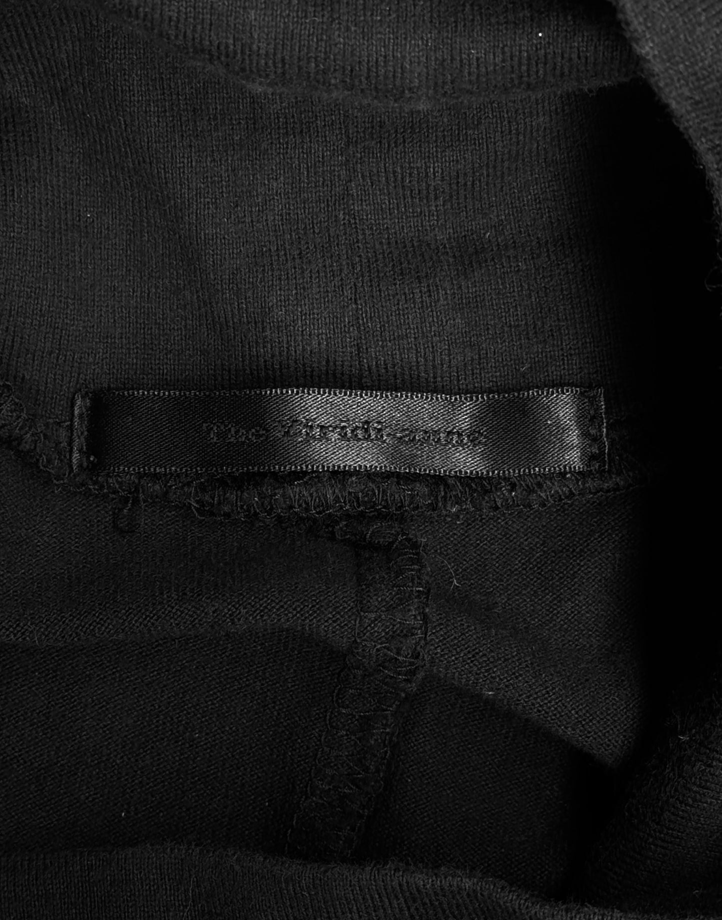 A close-up of a black fabric label sewn onto The Viridi-Anne Ninja High Neck Cotton Long-sleeves, showing medium size 2 and partially visible white text with minor fading on the black garment.