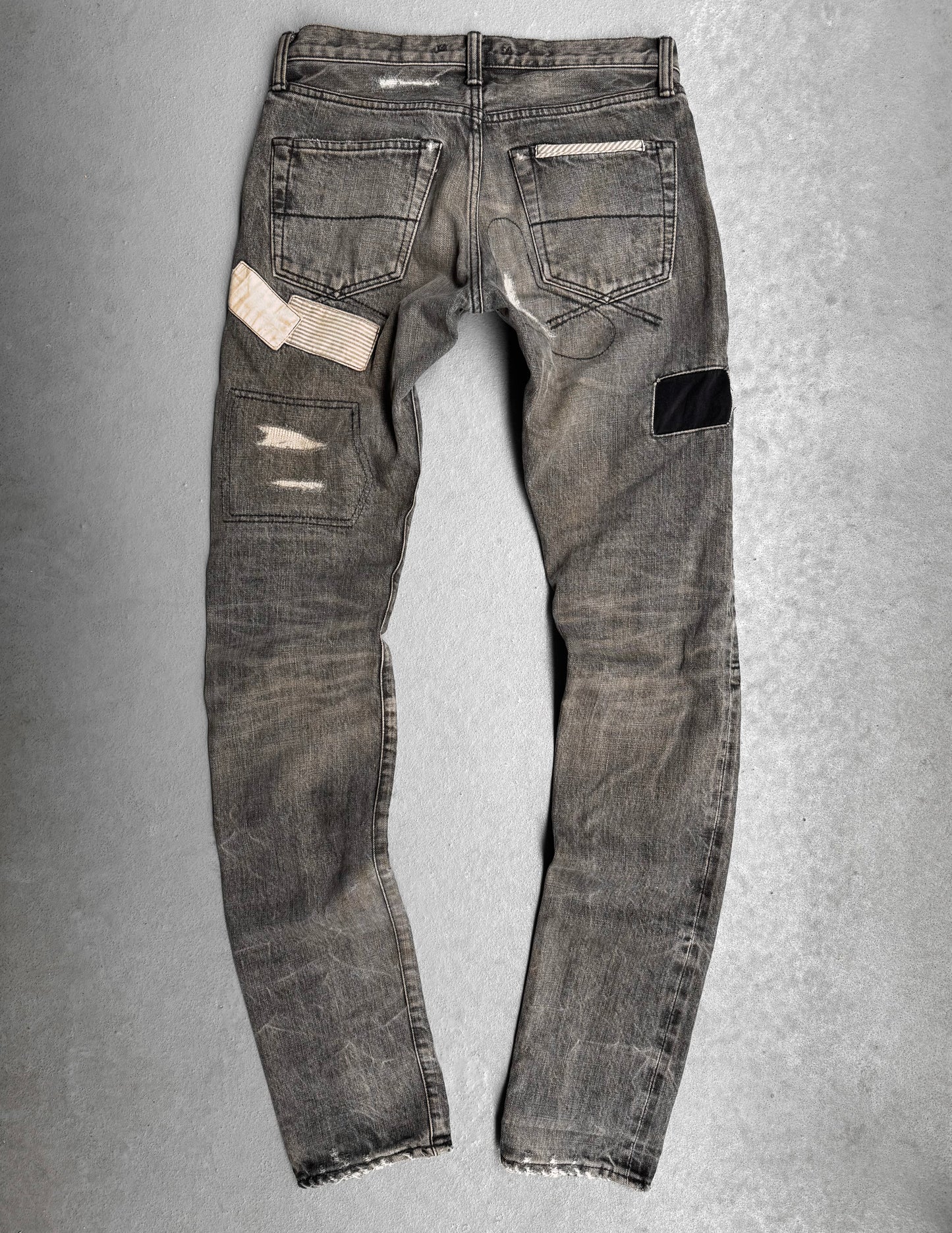 Mihara Yasuhiro AW10 Double-pockets Repair Patchwork Selvedge Denim—gray jeans featuring visible distressing, patch repairs (white striped, black), and frayed hems, ideal for a streetwear-inspired look.