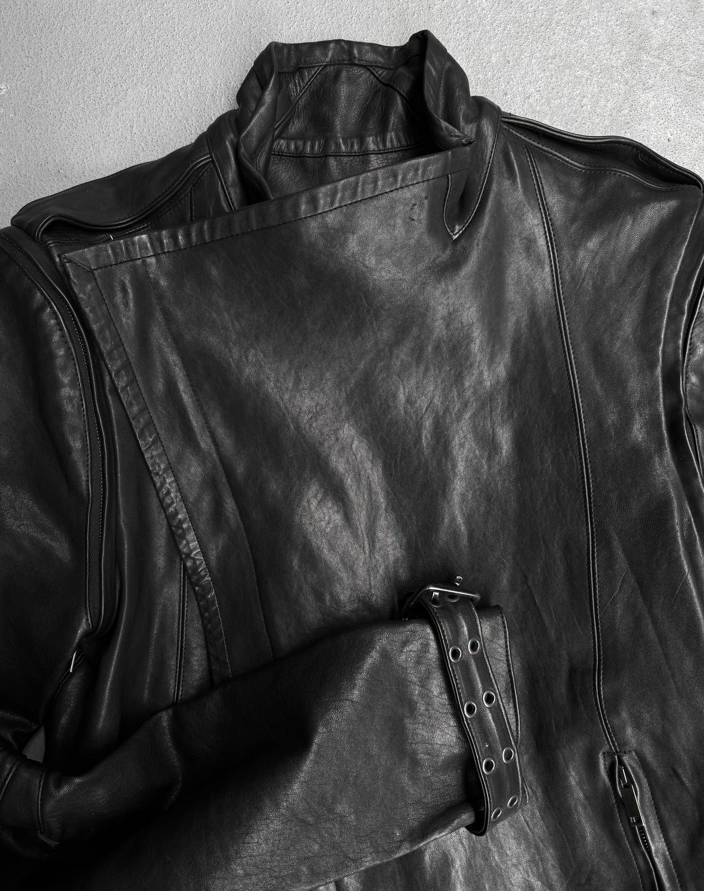 The Gareth Pugh AW09 Detachable Sleeves Horse Leather Riders Jacket, featuring an asymmetrical front zipper, shoulder epaulets, and a belted waist, is showcased laid flat on a light grey surface.