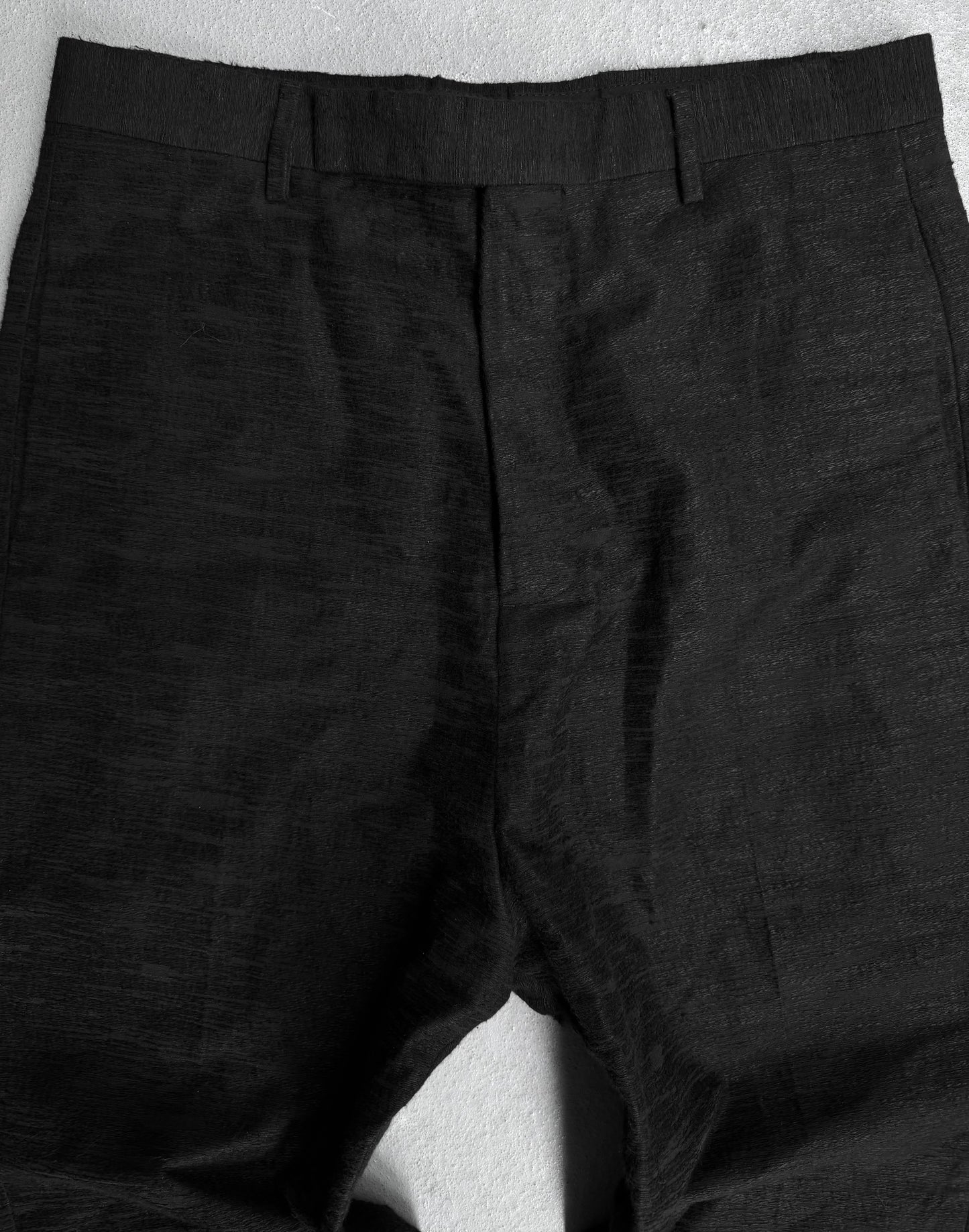 A close-up of Rick Owens SS17 “WALRUS” Radiant Woven Cropped Pants in black, IT 48 / US 32-33, laid flat on a light gray surface, displaying the textured waistband, belt loops, and upper legs.