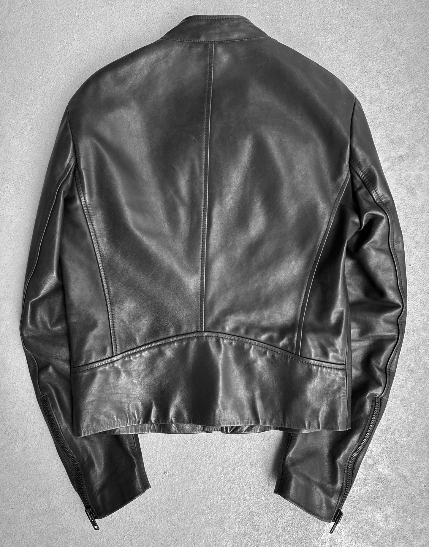 A Maison Martin Margiela AW10-11 Kokone Black Horse Leather 5-zip Jacket in size 44 is laid flat, back side up, on a light textured surface, displaying visible seams and sleeve zippers.