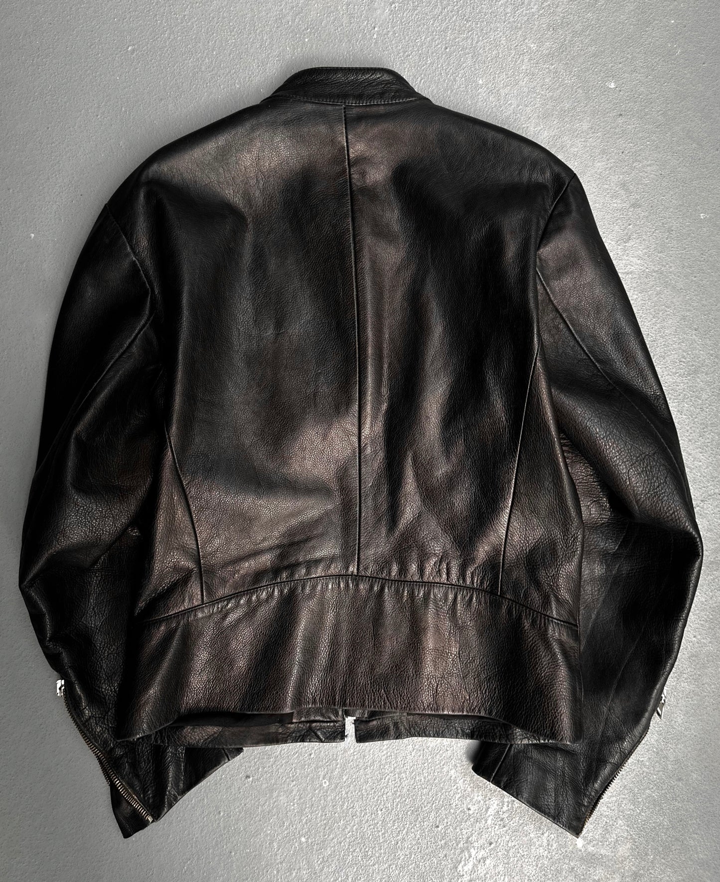 The Maison Martin Margiela AW00 Black Cowhide Leather 5-zip Rider Jacket lays flat on a gray surface, displaying the backs visible seams and subtle texture—a tribute to avant-garde fashion by Maison Martin Margiela.