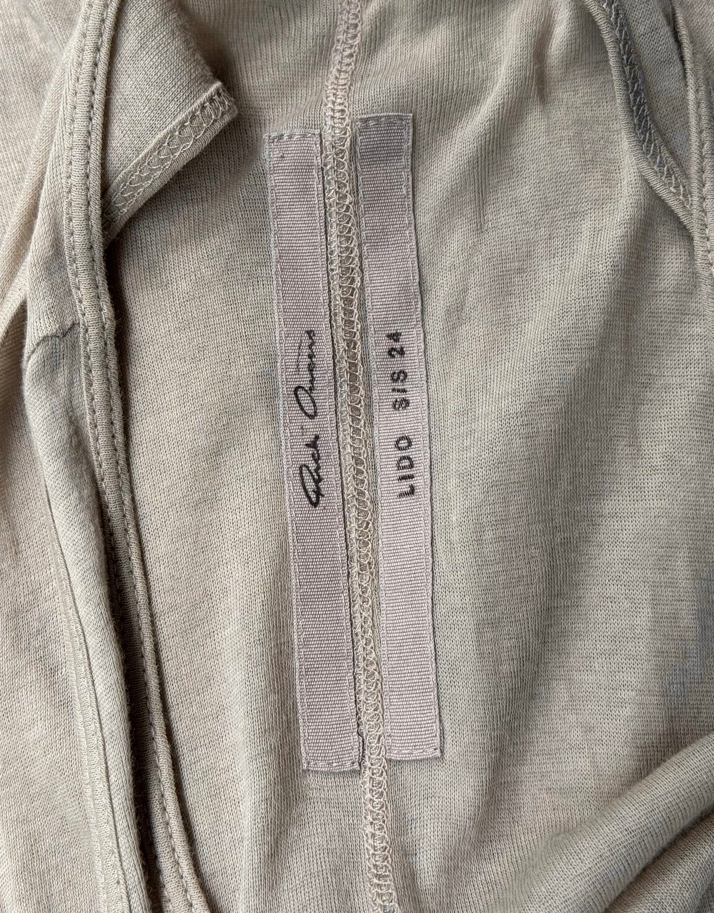 A pearl sheer tanks inner label features Rick Owens on one tag and LIDO SS24 with size SIS XS on the other, sewn onto the fabric—a subtle nod to avant-garde fashion’s attention to detail.