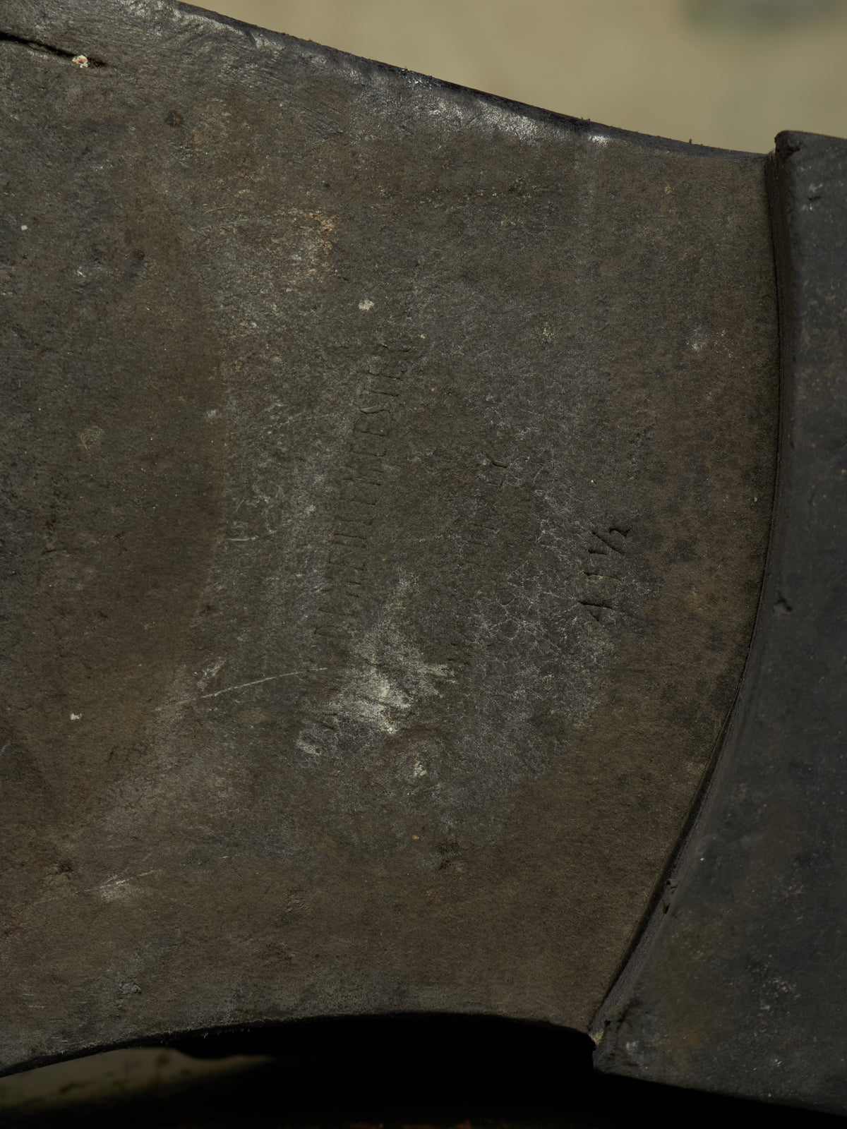 Close-up detail of a dark metal axe head showing the textured forge finish and bevel edge.