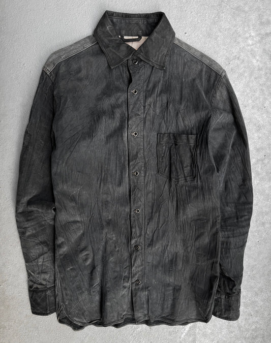 The Kyoji Maruyama Early 00s Washable Wrinkle Nubuck Leather Shirt is a black, long-sleeve button-up with a single chest pocket, shown slightly wrinkled and laid flat on a light gray textured surface.