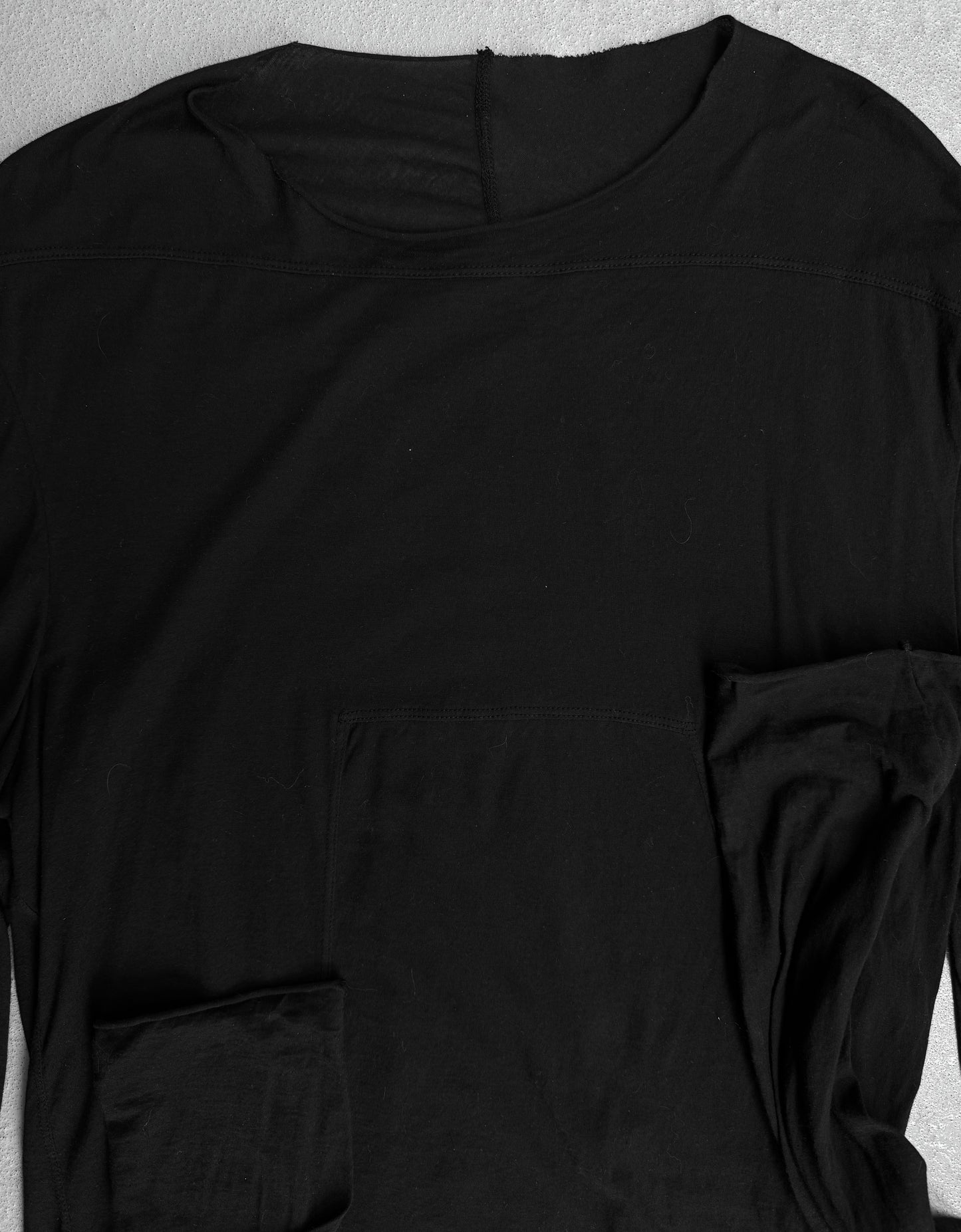 The Rick Owens DRKSHDW AW24 “PORTERVILLE” Geometric Level Long-sleeve shirt, in black with a round neckline, is laid flat on a light surface; its slightly wrinkled fabric and partially folded sleeve hint at subtle, modern style.