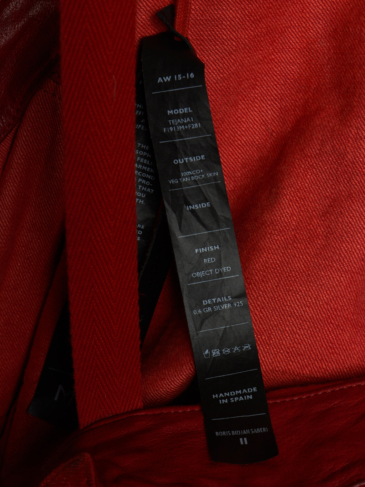 A close-up shot of a black hangtag attached to a red textured fabric garment, showing printed specifications on the tag.