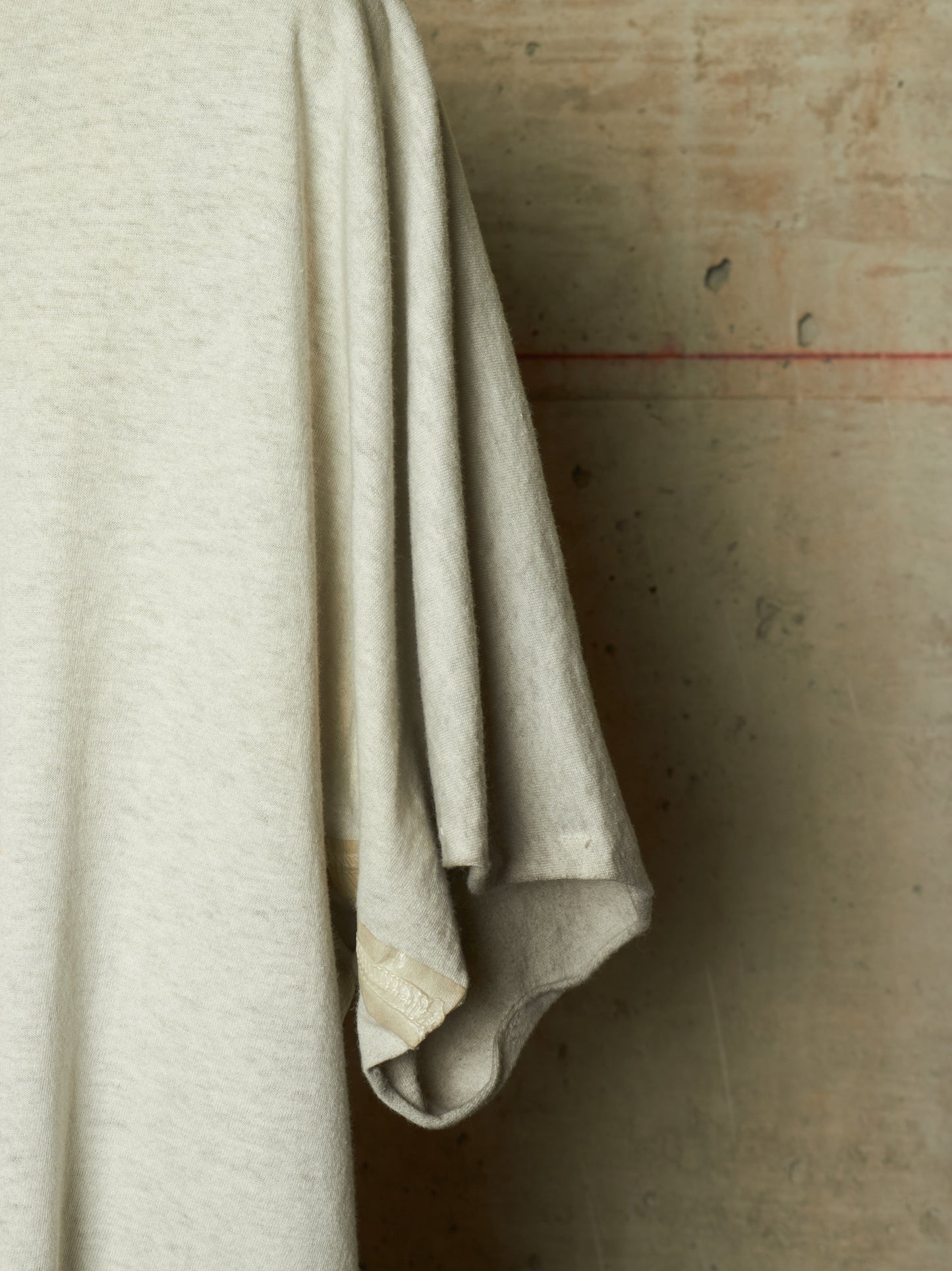 A close-up of a light beige or off-white knit fabric draped vertically against a textured concrete wall.