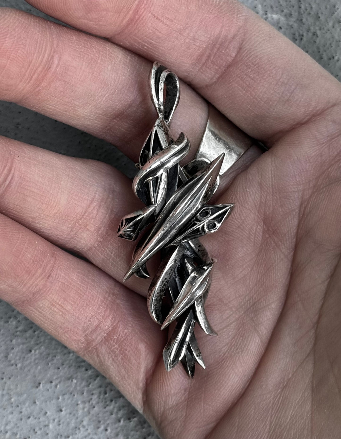 A BLESS M’s COLLECTION Early 00s Silver Arabesque Cross Pendant with sharp, angular, intertwined forms rests in an open palm. With intricate leaf-like details, it embodies the brands dedication to sustainability and innovation.