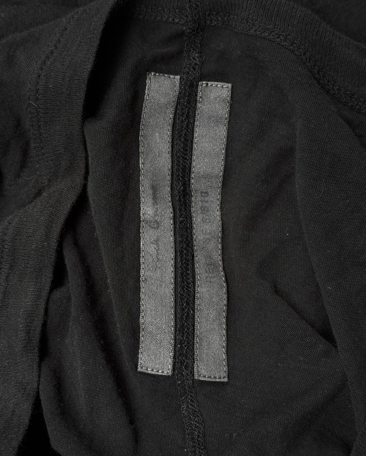 A close-up of the interior of a Rick Owens SS10 “RELEASE” Black Sheer Long-sleeves, highlighting a vertical seam and two slim black fabric tags sewn side by side—a signature touch in Rick Owens avant-garde style.