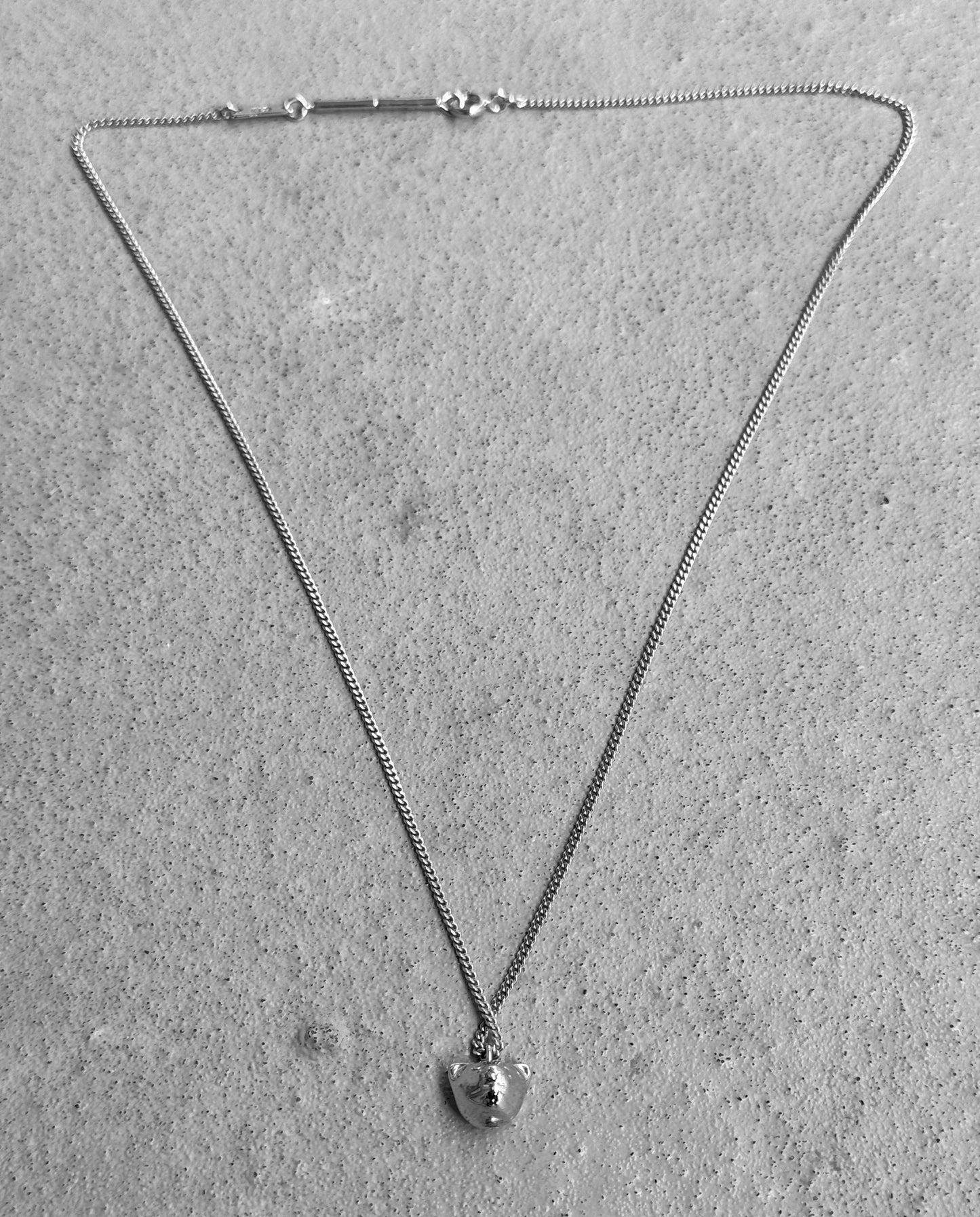 On a textured surface rests a delicate chain necklace with a small teddy bear pendant, showcasing the signature detail of DIOR HOMME. Its as striking as their early 00s collection, echoing the boldness of silver-painted skinny jeans.