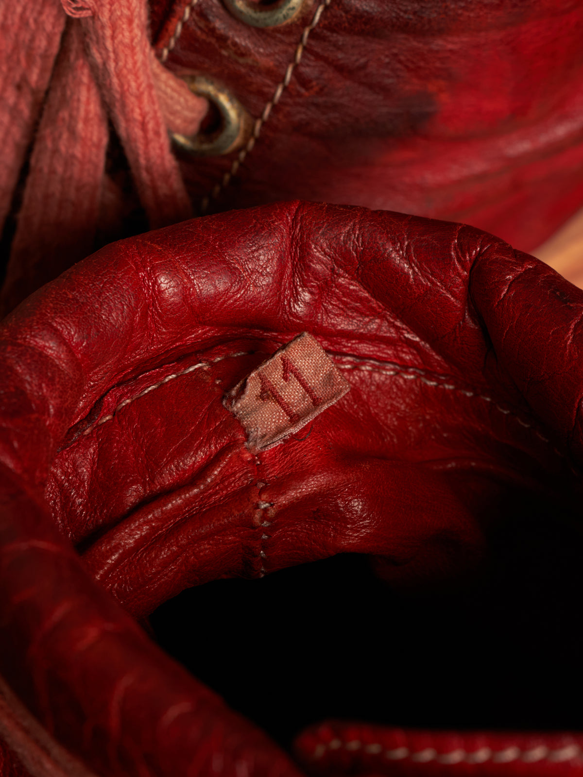 Close-up of a red leather boot or shoe interior with visible stitching, lace eyelets, and a small sewn label.