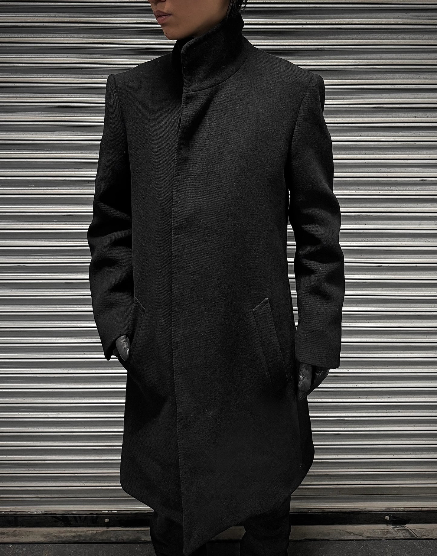 Person wearing a black coat standing in front of a metallic shutter.