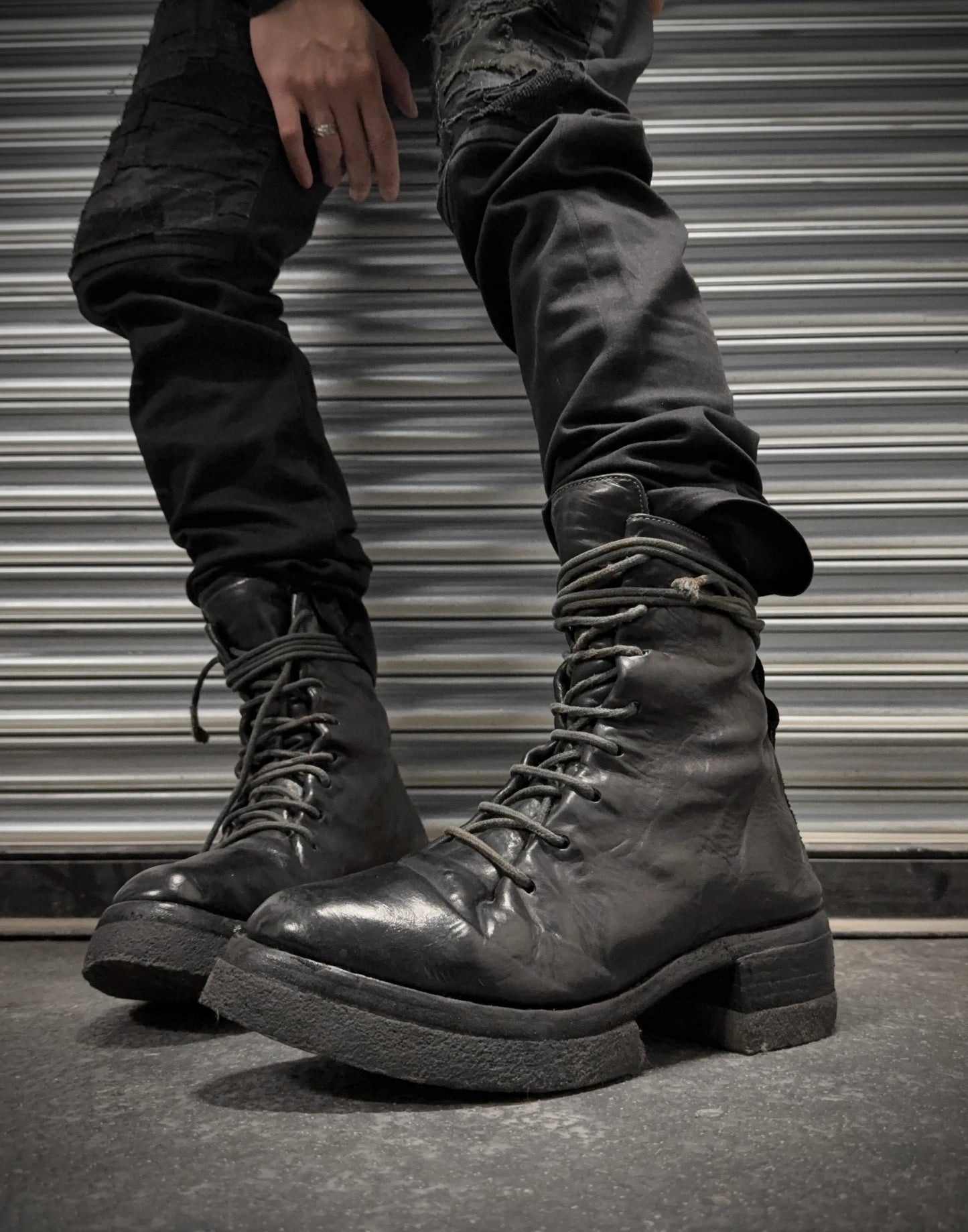 Black leather boots worn with dark pants against a metallic shutter background