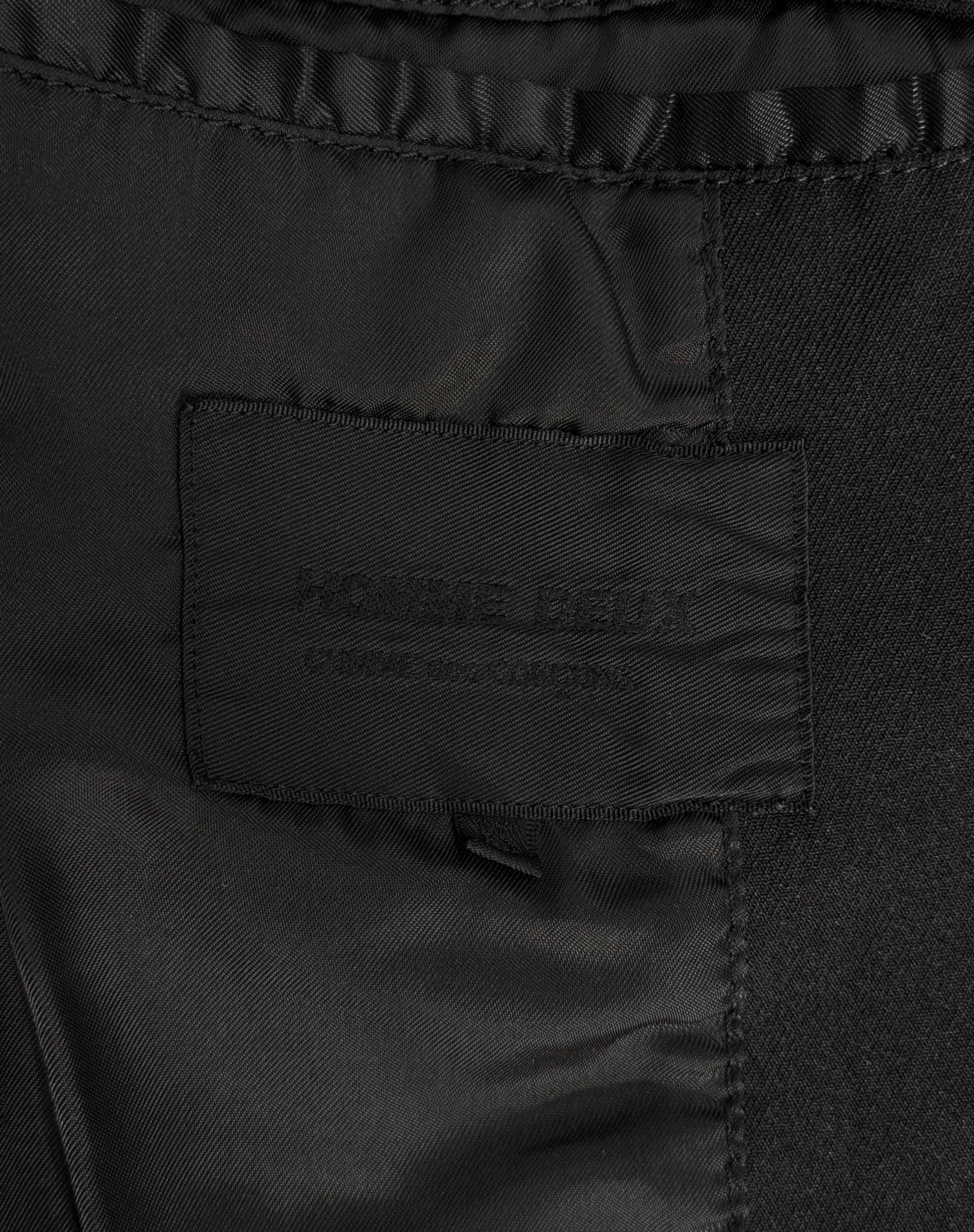 Close-up of a black clothing tag on dark fabric, subtly embroidered with text, hinting at its avant-garde fashion roots, reminiscent of iconic menswear labels like the COMME des GARÇONS HOMME DEUX Early 00s Reversible Button-up Coat by COMME des GARÇONS.
