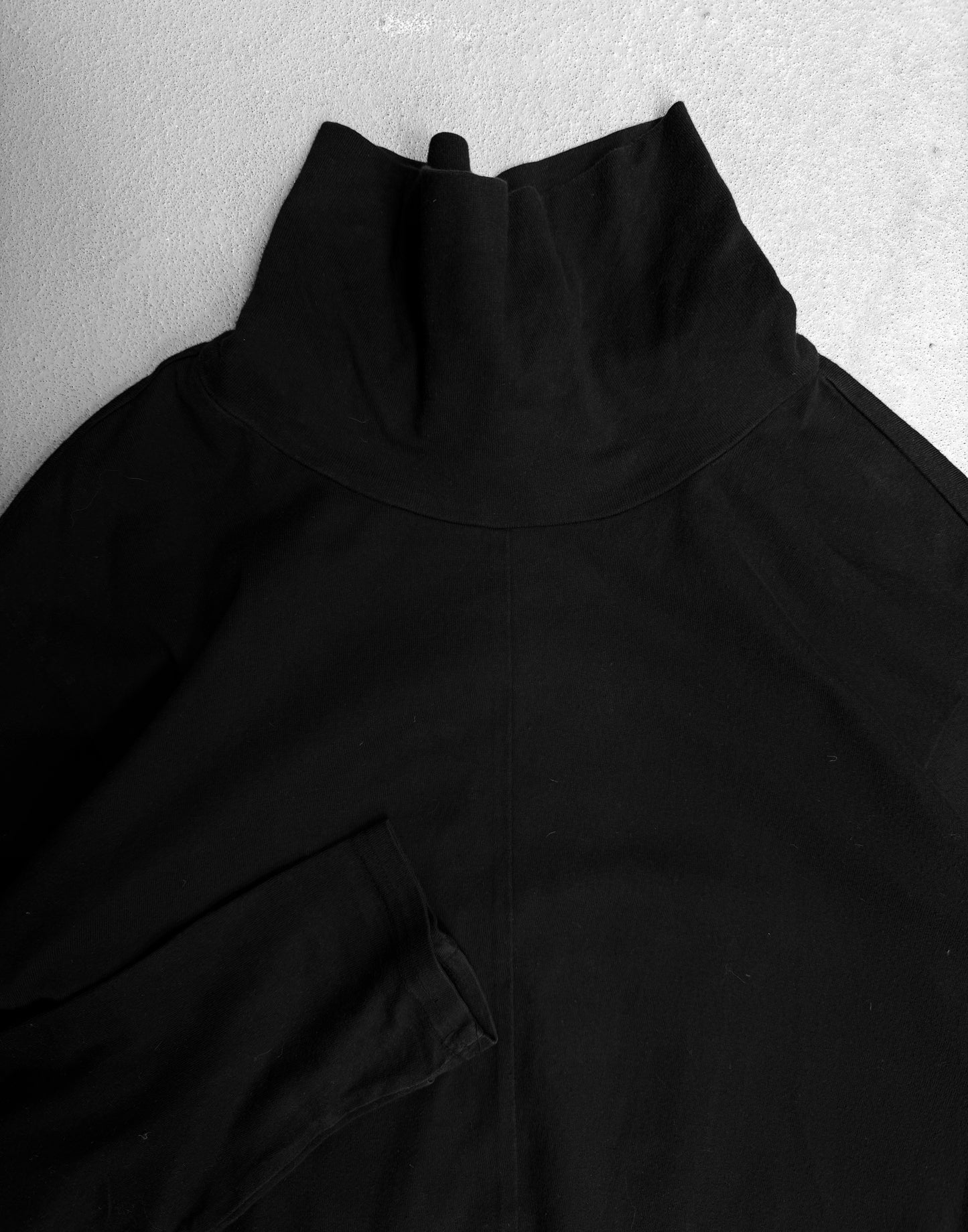 The Viridi-Anne Ninja High Neck Cotton Long-sleeves in black, size 2 (medium), laid flat on a light surface with one sleeve partially visible and the folded high collar featured; minor fading shown.