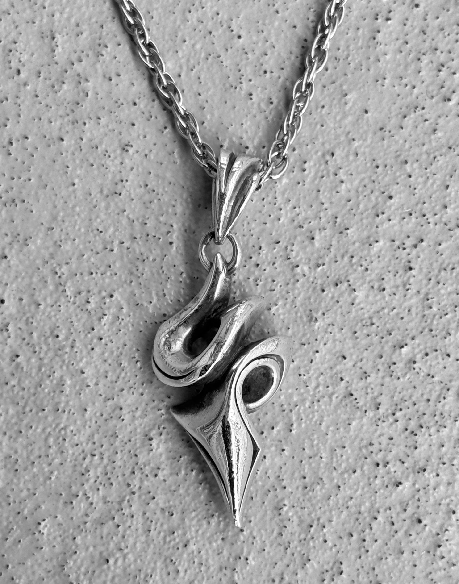 The BLESS M’s Collection (BLESS) Early 00s Silver Tribal Twist Pendant Chain features an abstract pendant with swirling shapes, a polished finish, and a textured chain. The sustainability focus is highlighted by a speckled stone backdrop for added elegance.