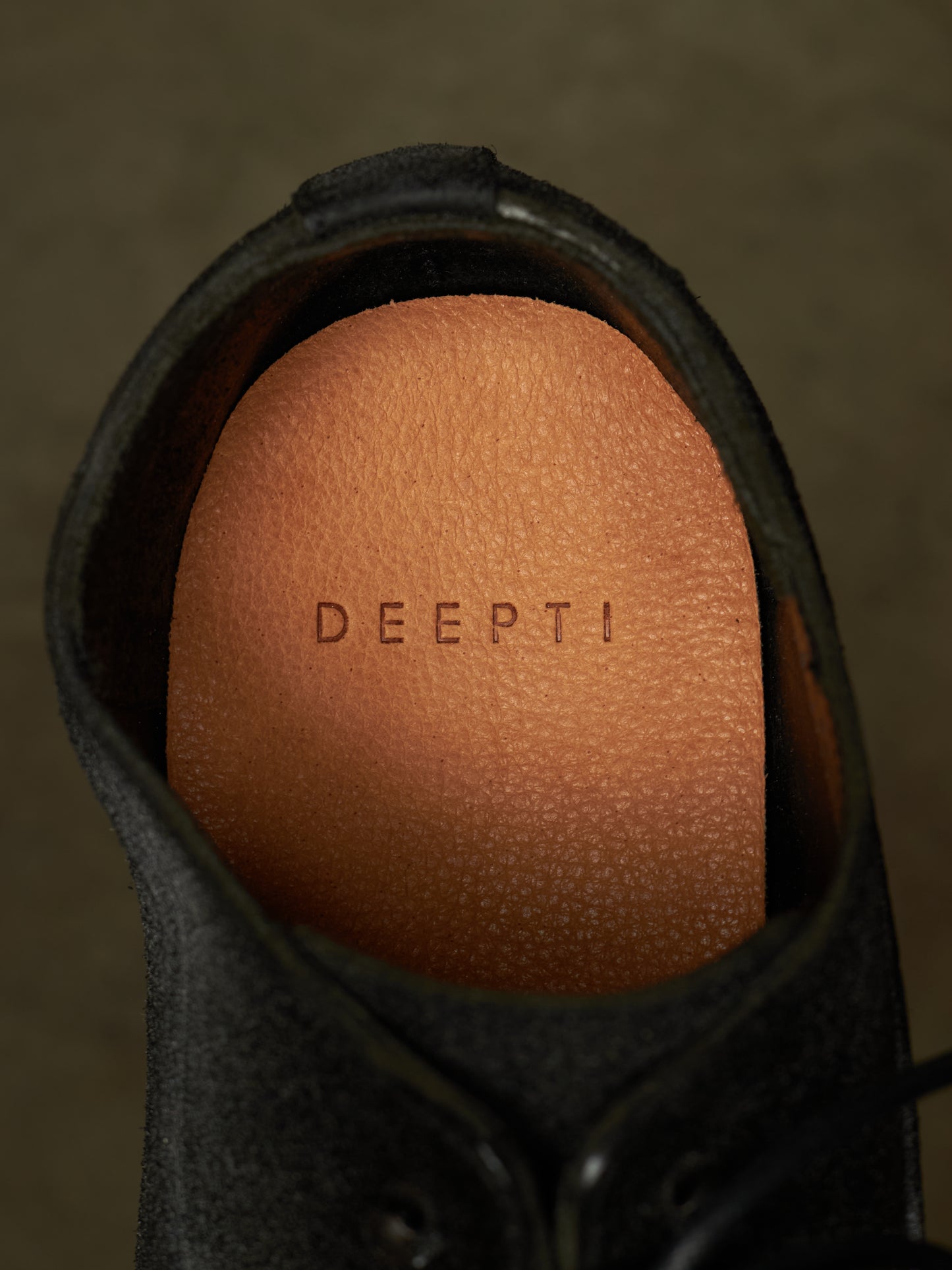 Close-up of the interior of a dark gray or black shoe, showing a tan textured footbed with the brand name 'DEEPTI' embossed on it.