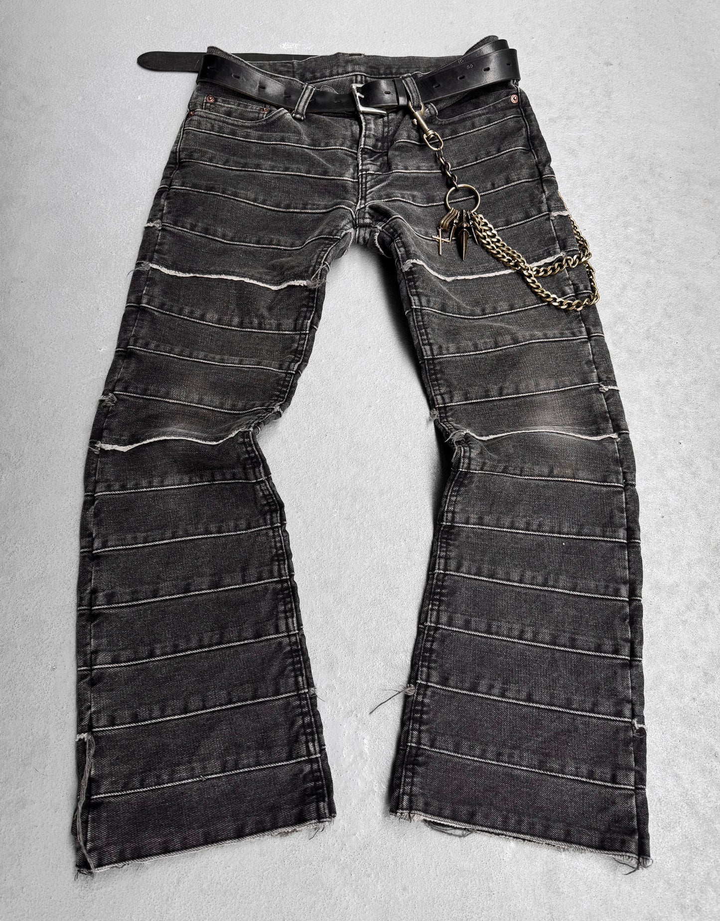 These Hysteric Glamour Early 00s ‘Kinky’ Grey Flare Hagi Denim exude punk rock fashion with black denim featuring horizontal stitched stripes, a belt, chain charms, frayed hem, and slight fading reminiscent of the brands edgy style.