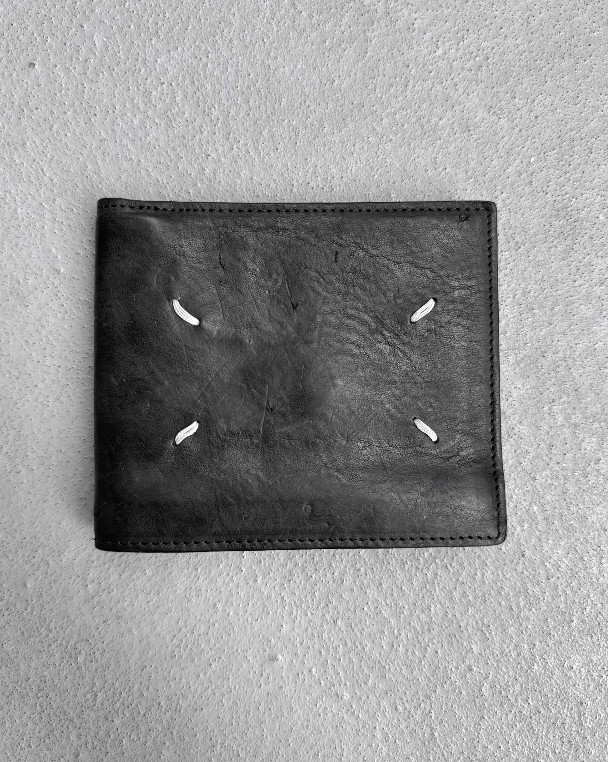 Maison Martin Margiela AW15 Distressed Calfskin Leather Bi-fold Wallet in black, OneSize, with four white stitches in a square, condition 8/10 and slightly used, shown on a textured gray surface.