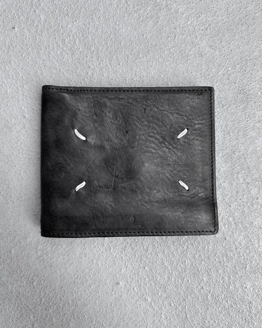 Maison Martin Margiela AW15 Distressed Calfskin Leather Bi-fold Wallet in black, OneSize, with four white stitches in a square, condition 8/10 and slightly used, shown on a textured gray surface.