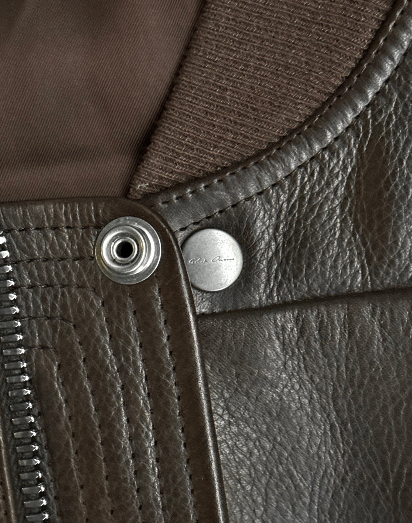 Close-up of the Rick Owens AW23 LUXOR Girdered Leather Bomber Jacket in brown calfskin, highlighting the metal snap button, zipper, and textured ribbed collar with brown fabric lining.