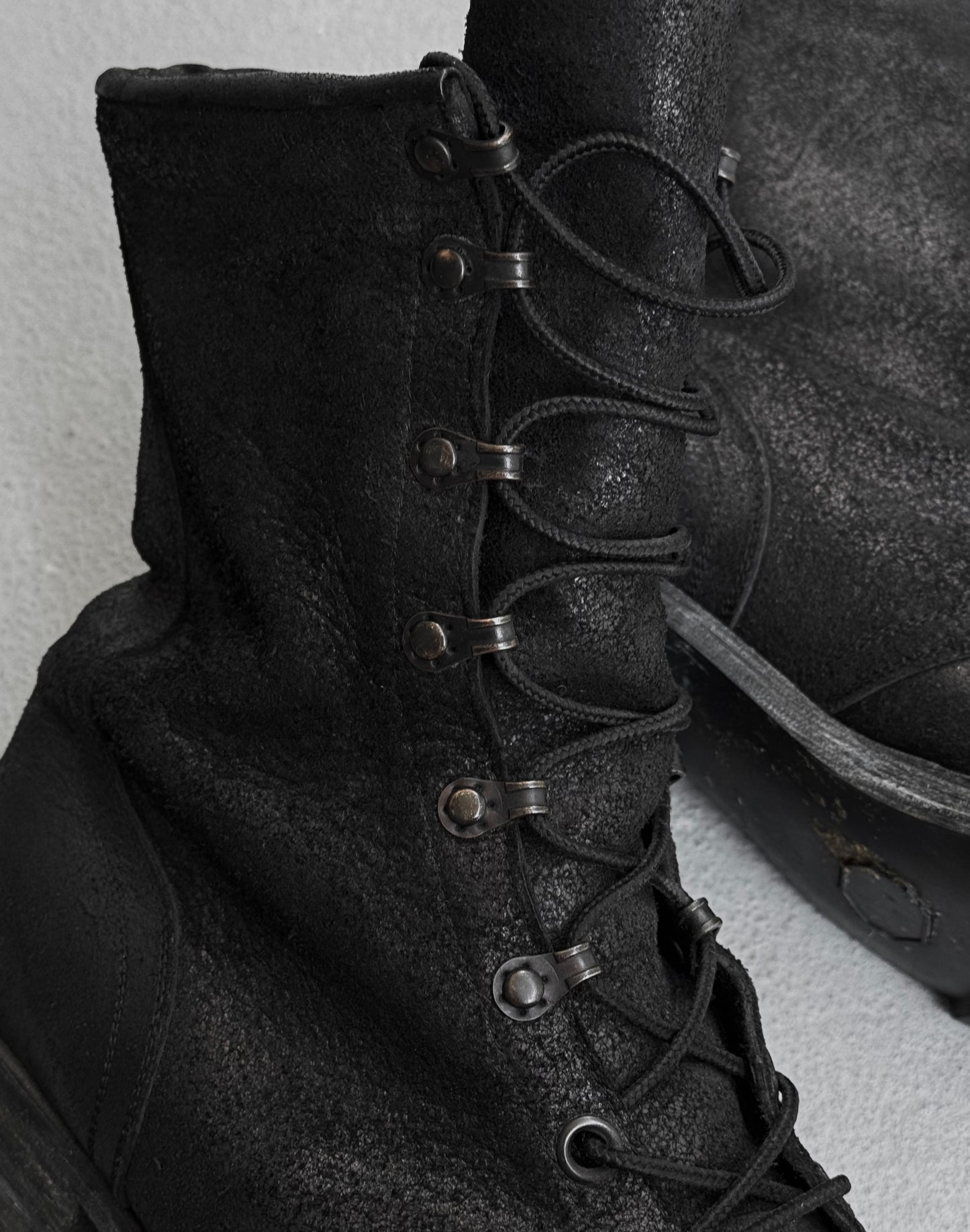 Close-up of ATTACHMENT by Kazuyuki Kumagai Reversed Cow Leather Lace-up Boots: rugged black military-inspired boots with metal eyelets and textured, worn details—ideal for adding edge to modern menswear.